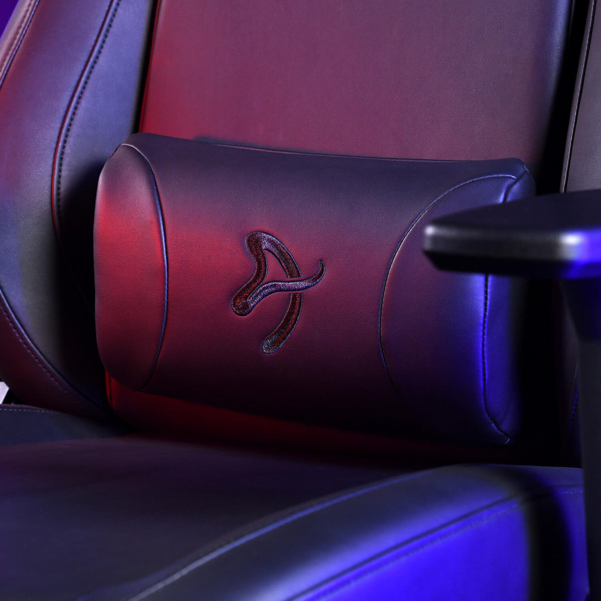 A black leather chair with a logo on a cushion, lit by blue and red light.