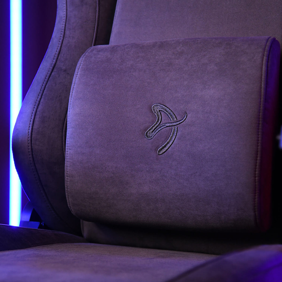 Close-up of a brown suede chair with a curved design and stitched logo on the cushion.