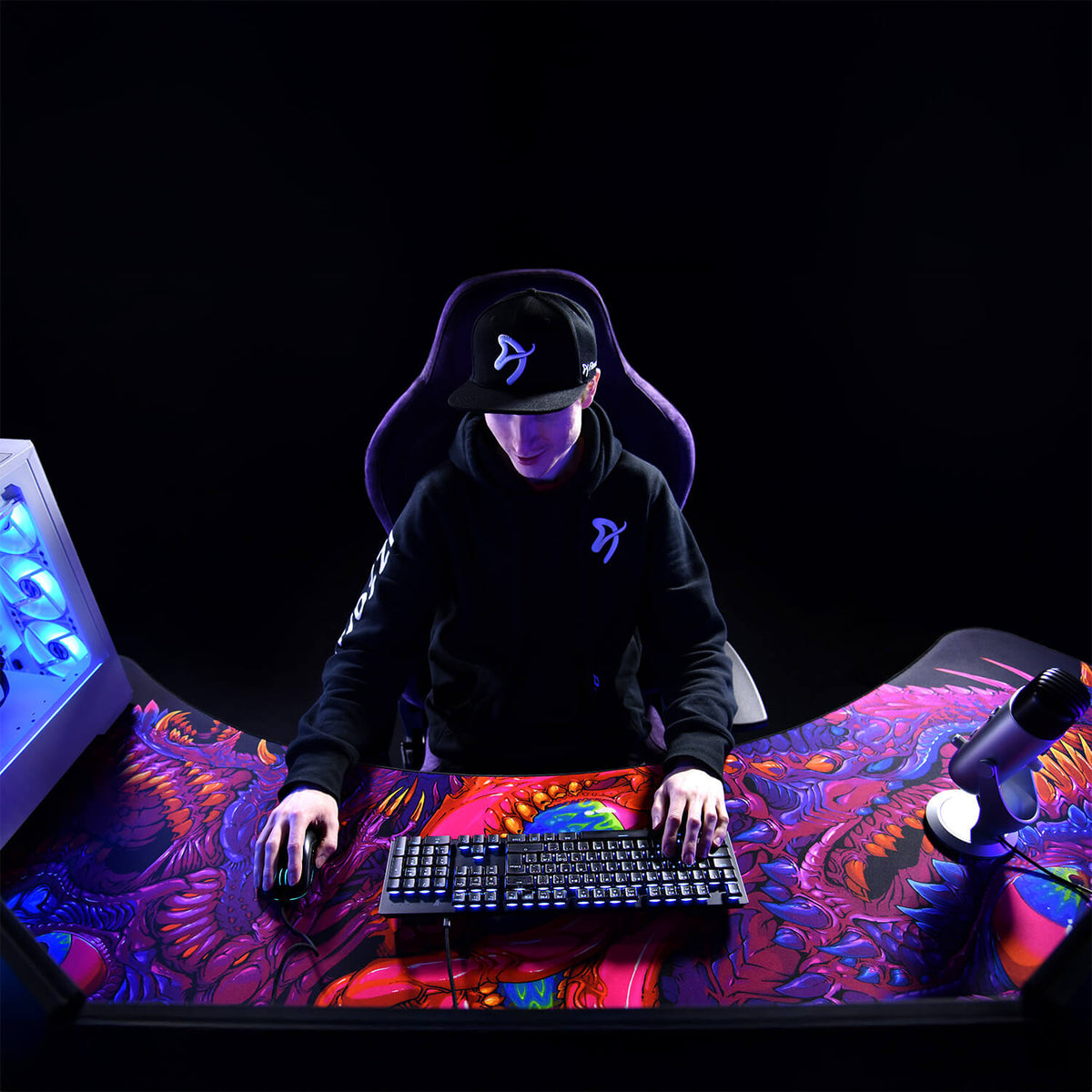Gamer at an Arena Angelo corner desk by Arozzi Europe with keyboard, mouse, PC, and mic.