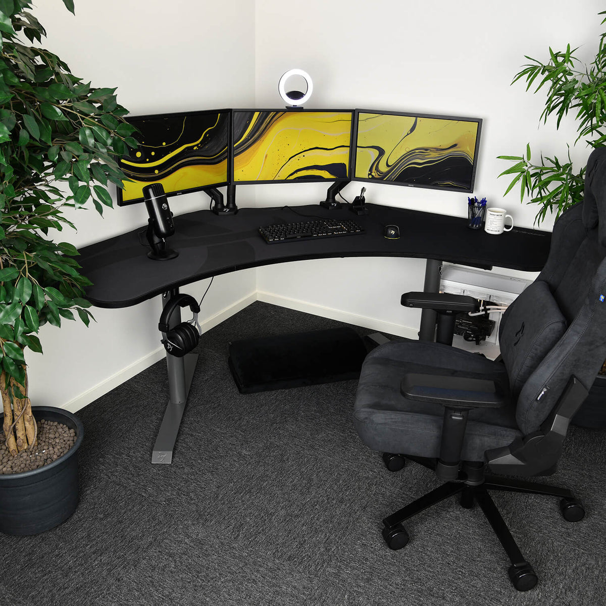 Arozzi Europe Arena Angelo corner desk with triple monitors, mic, plant, and webcam ring light.