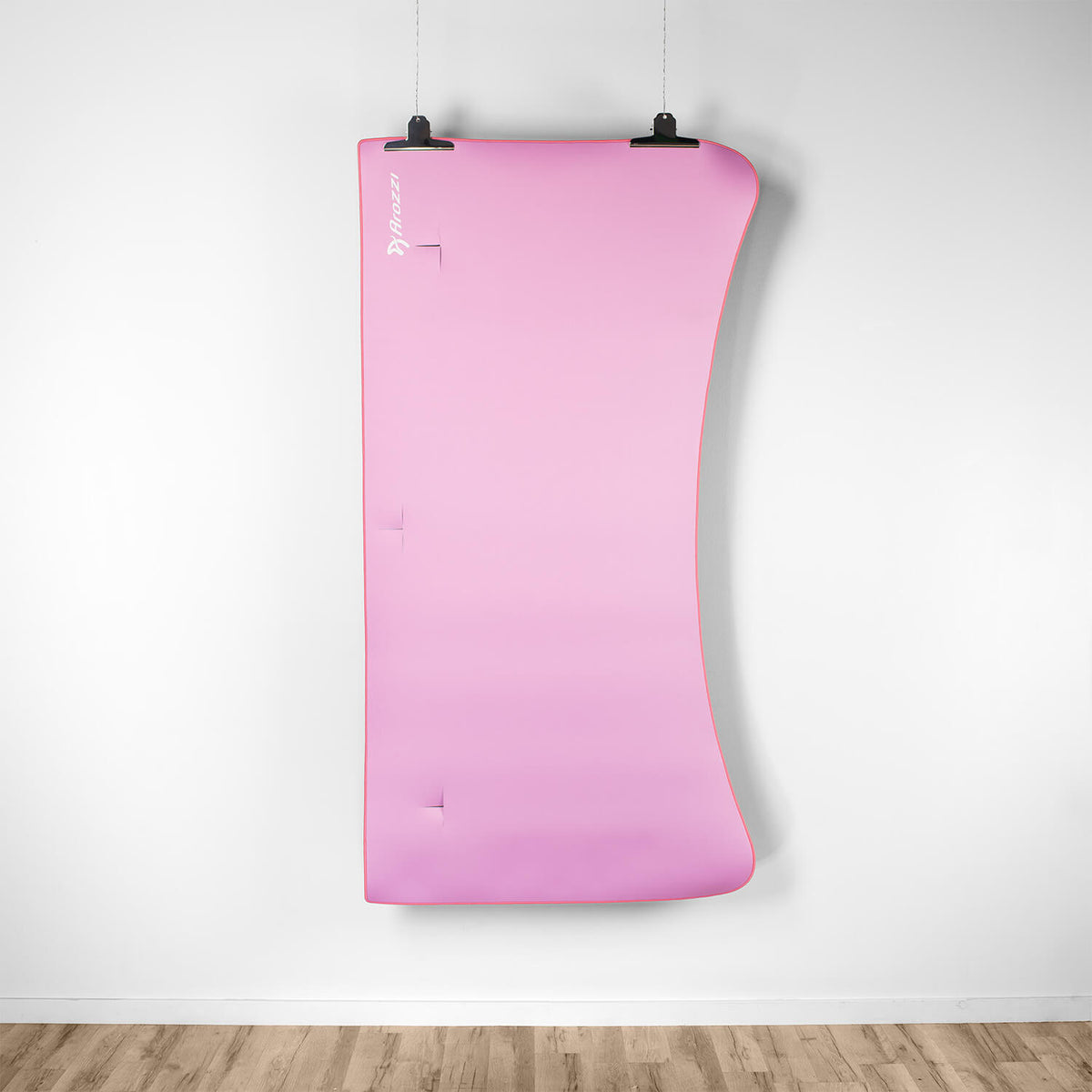 Arozzi Europe Arena Mousepad, pink and irregular, hangs on a white wall above a wood floor.