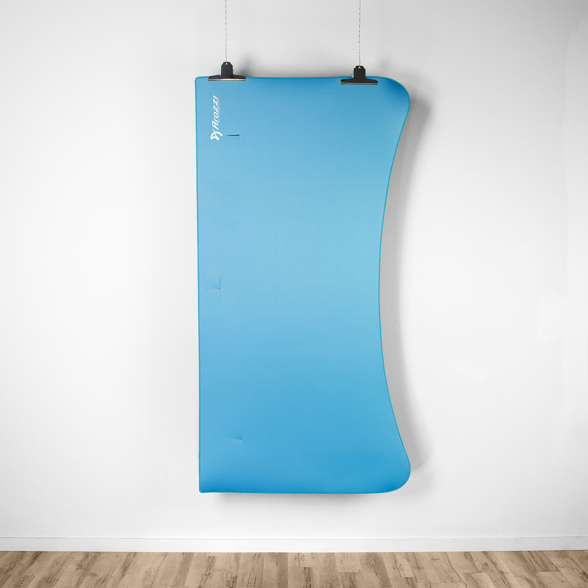 A large blue Arozzi Europe Arena Mousepad hangs vertically on a white wall above wood flooring.