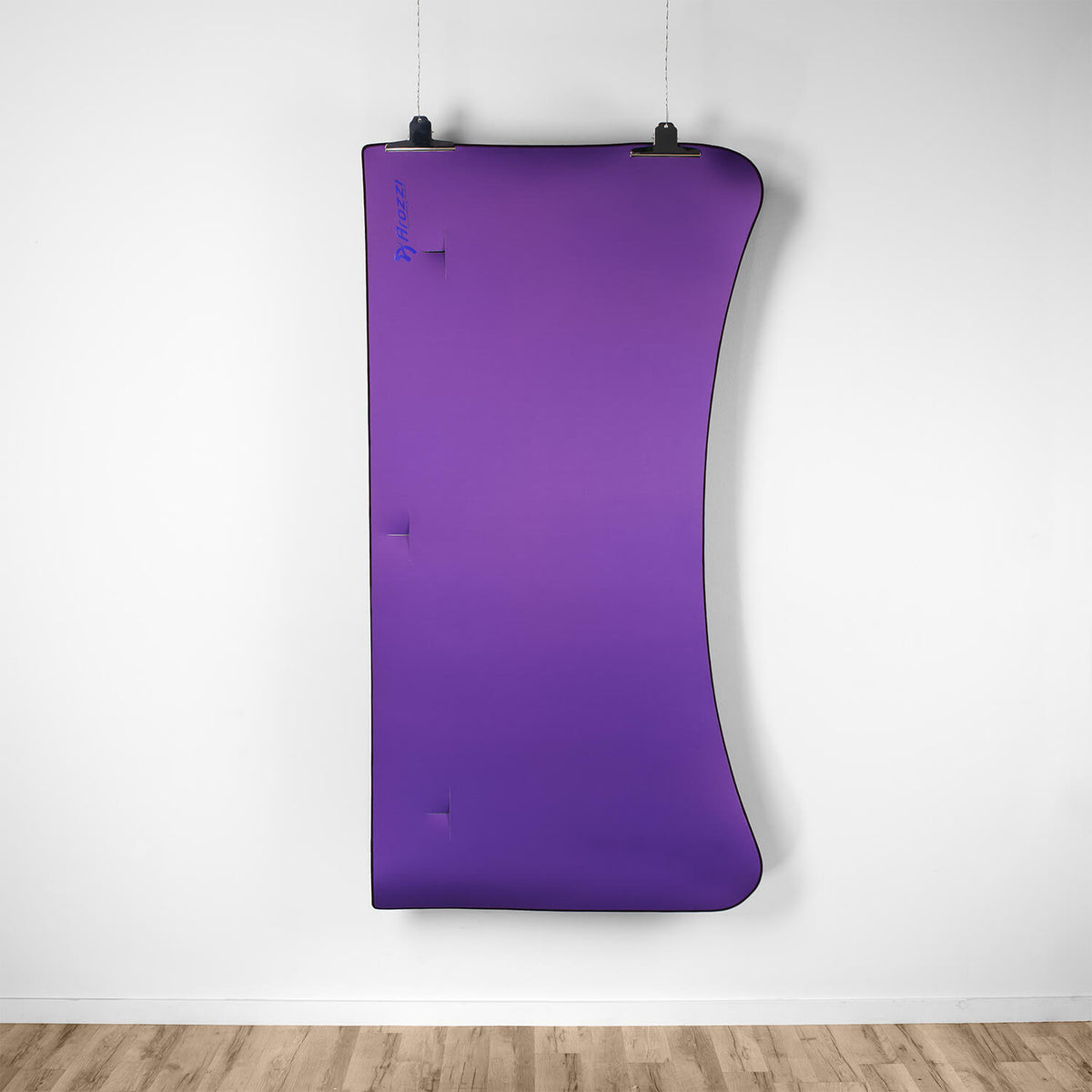 A purple, curved Arozzi Europe Arena Mousepad hangs on a white wall above a wooden floor.