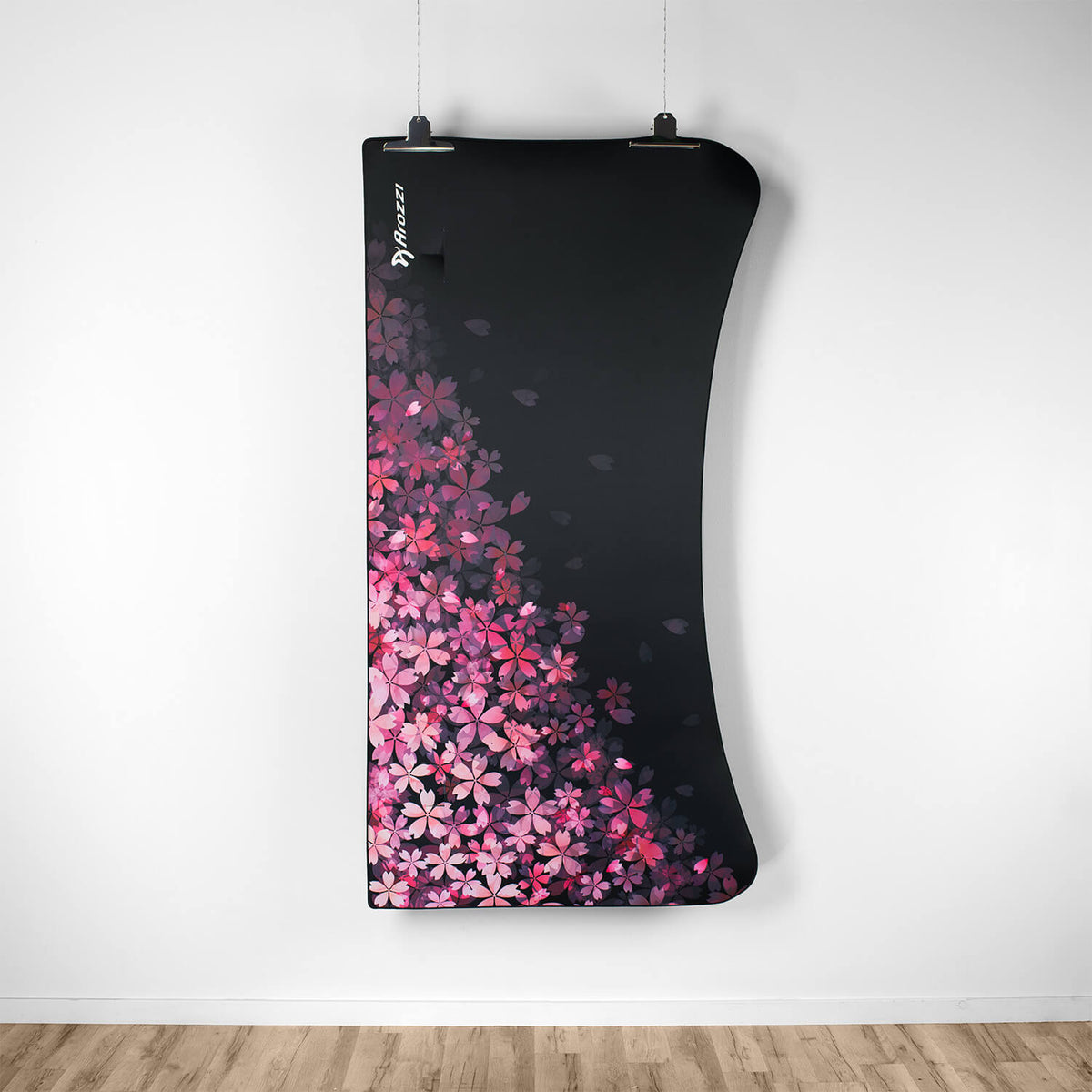 Curved black Arozzi Europe Arena Mousepad with pink cherry blossoms, hanging on a white wall.