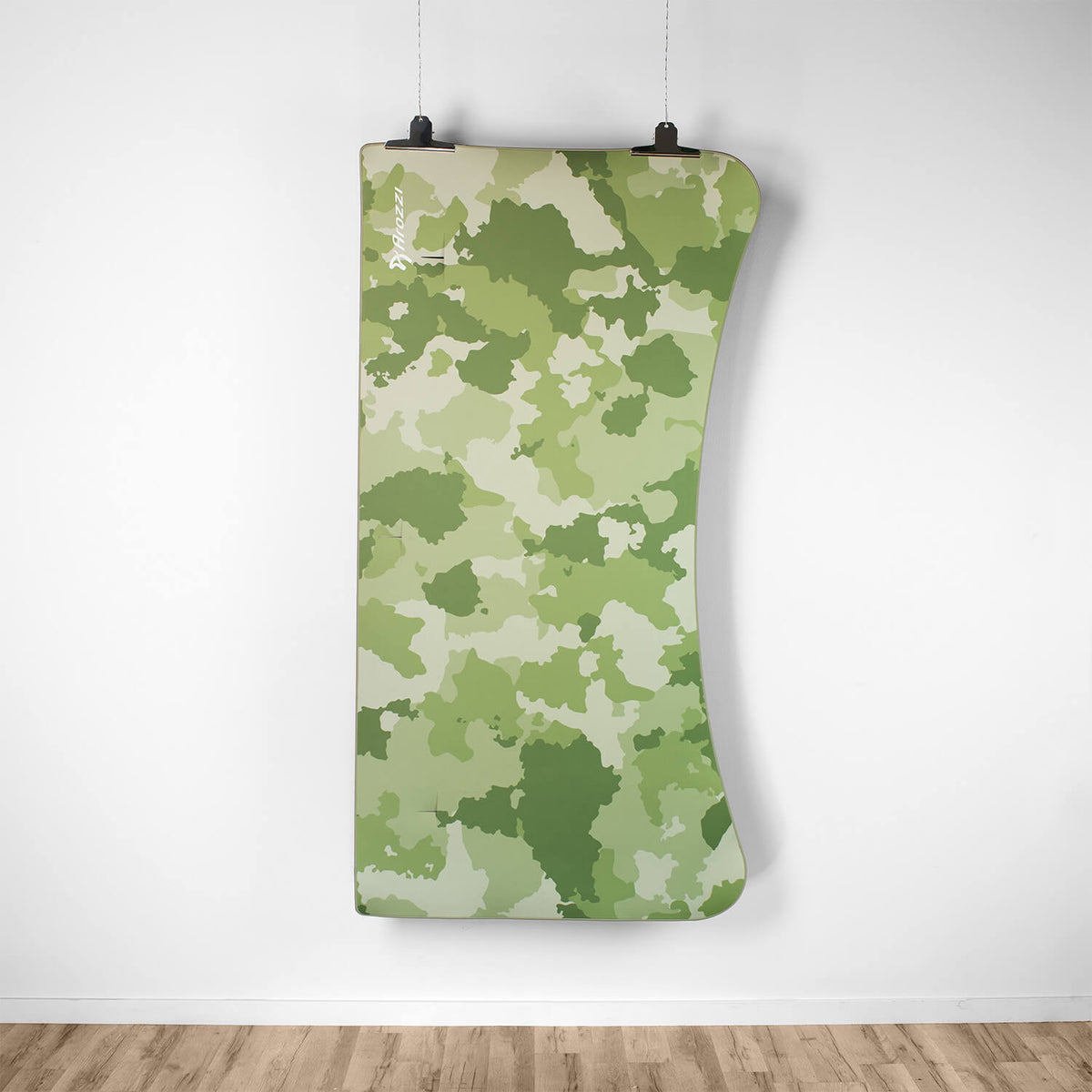 Arozzi Europe Arena Mousepad in curved green camo hangs on a white wall above wooden floor.