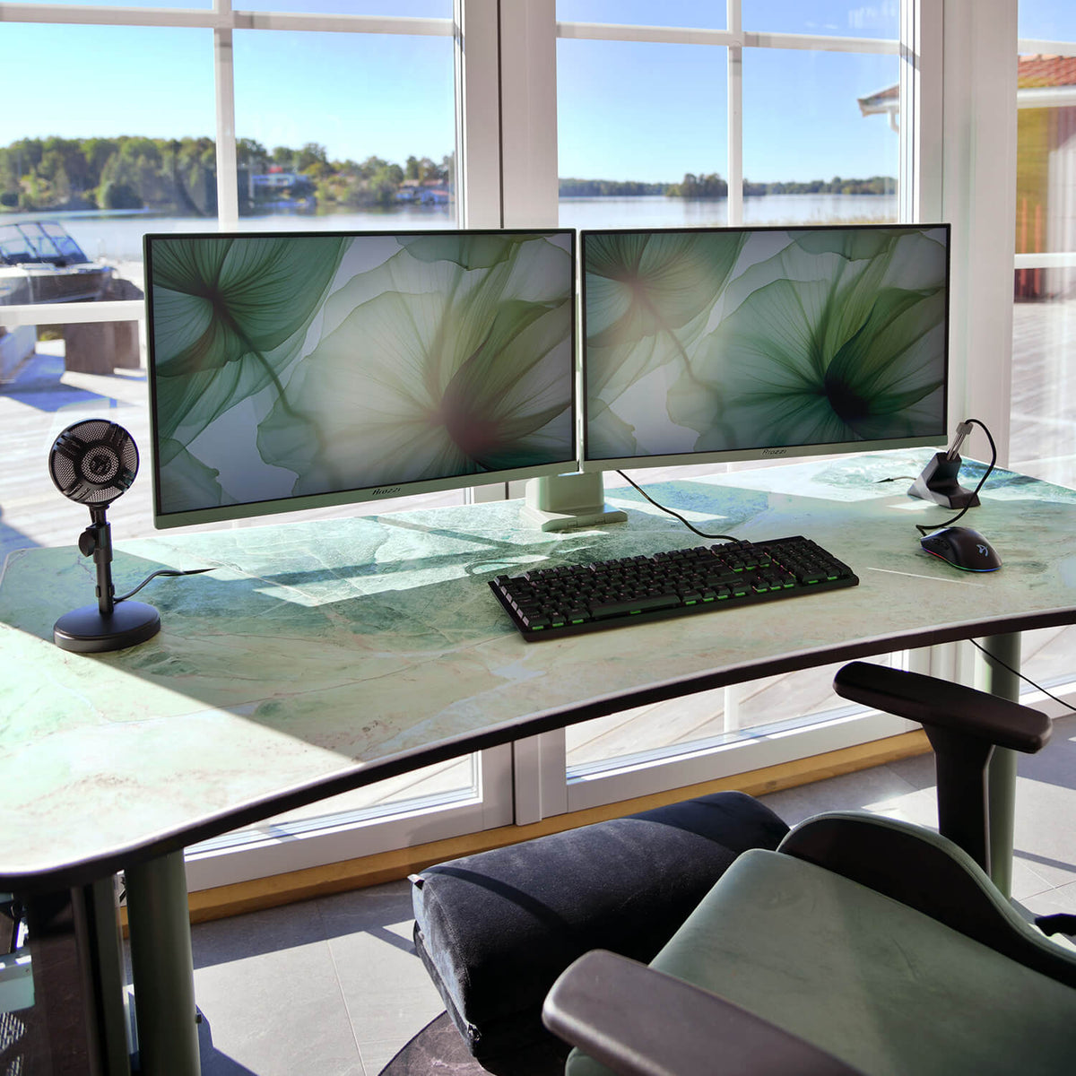 Dual monitors on a curved desk by a window, with an Arozzi Arena Mousepad and microphone.