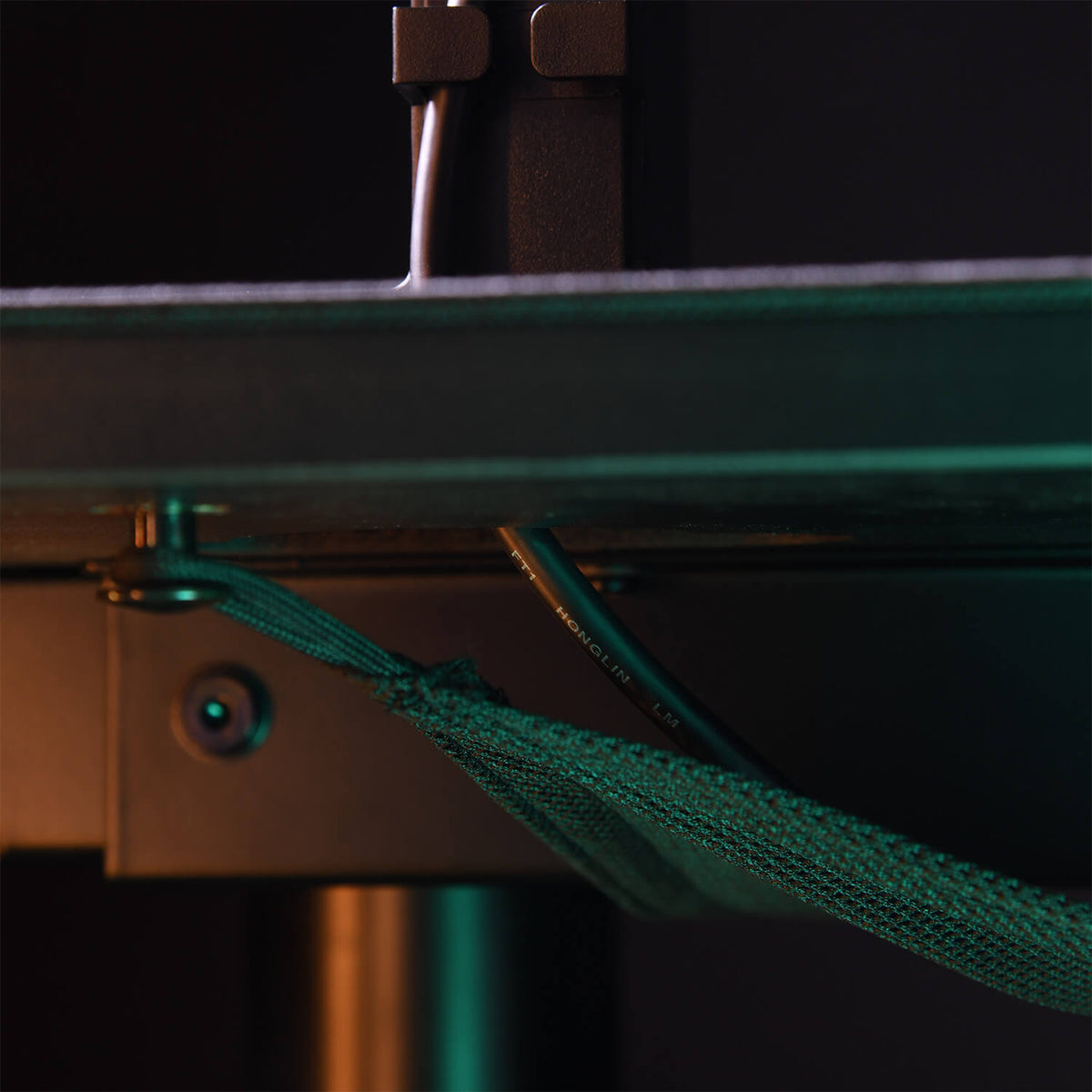 Close-up of a green strap and cable secured under a metal table or shelf with screws.