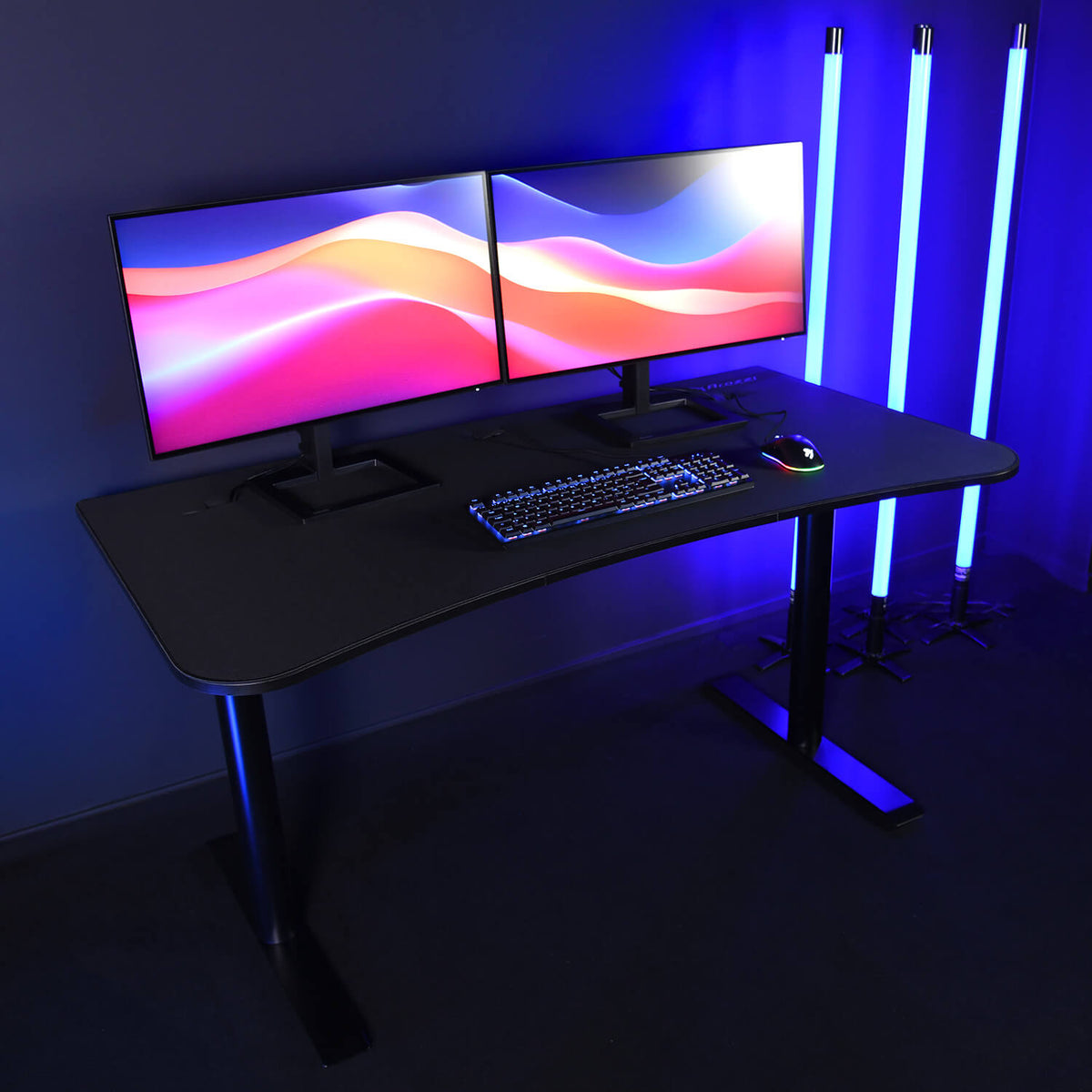 Arozzi Arena Gaming Desk - Medium holds dual monitors, keyboard, mouse, and blue LED lights.