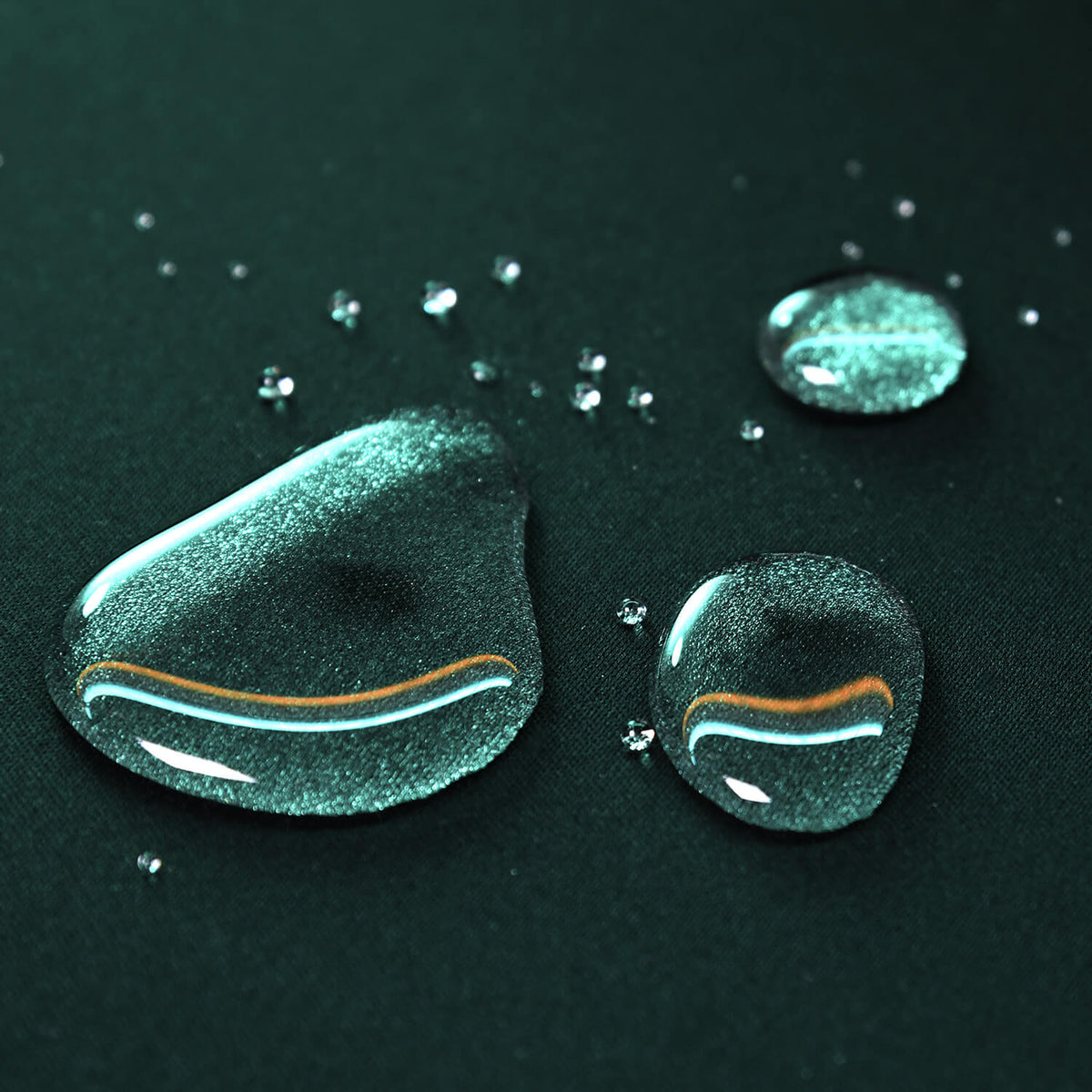 Water droplets and small beads on a dark green water-resistant fabric surface.