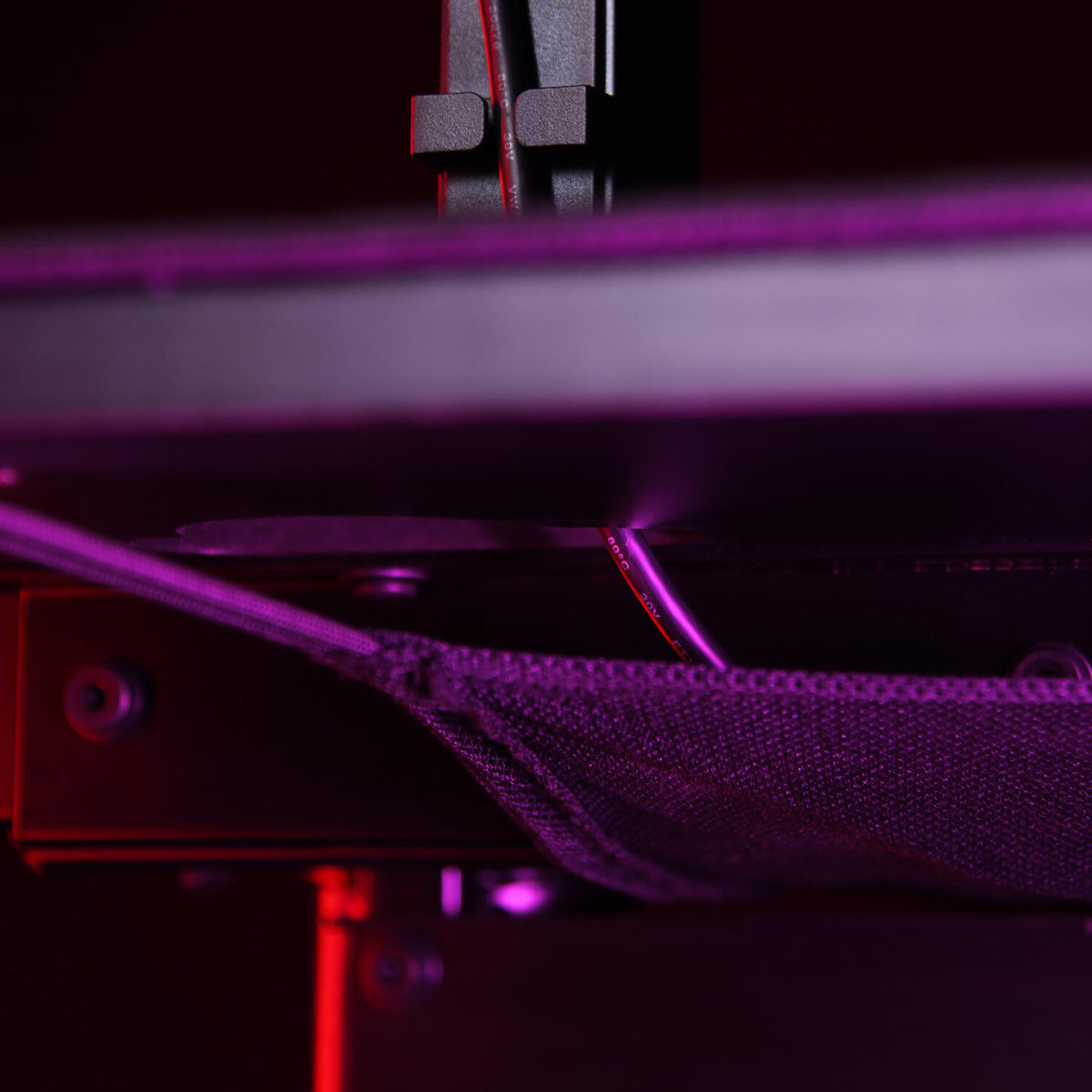 Close-up of a 3D printer part with purple and red lighting, showing wires and mesh cover.