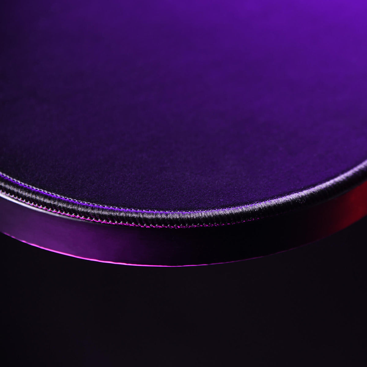 Close-up of a round, purple tabletop with dramatic lighting and a glossy edge.