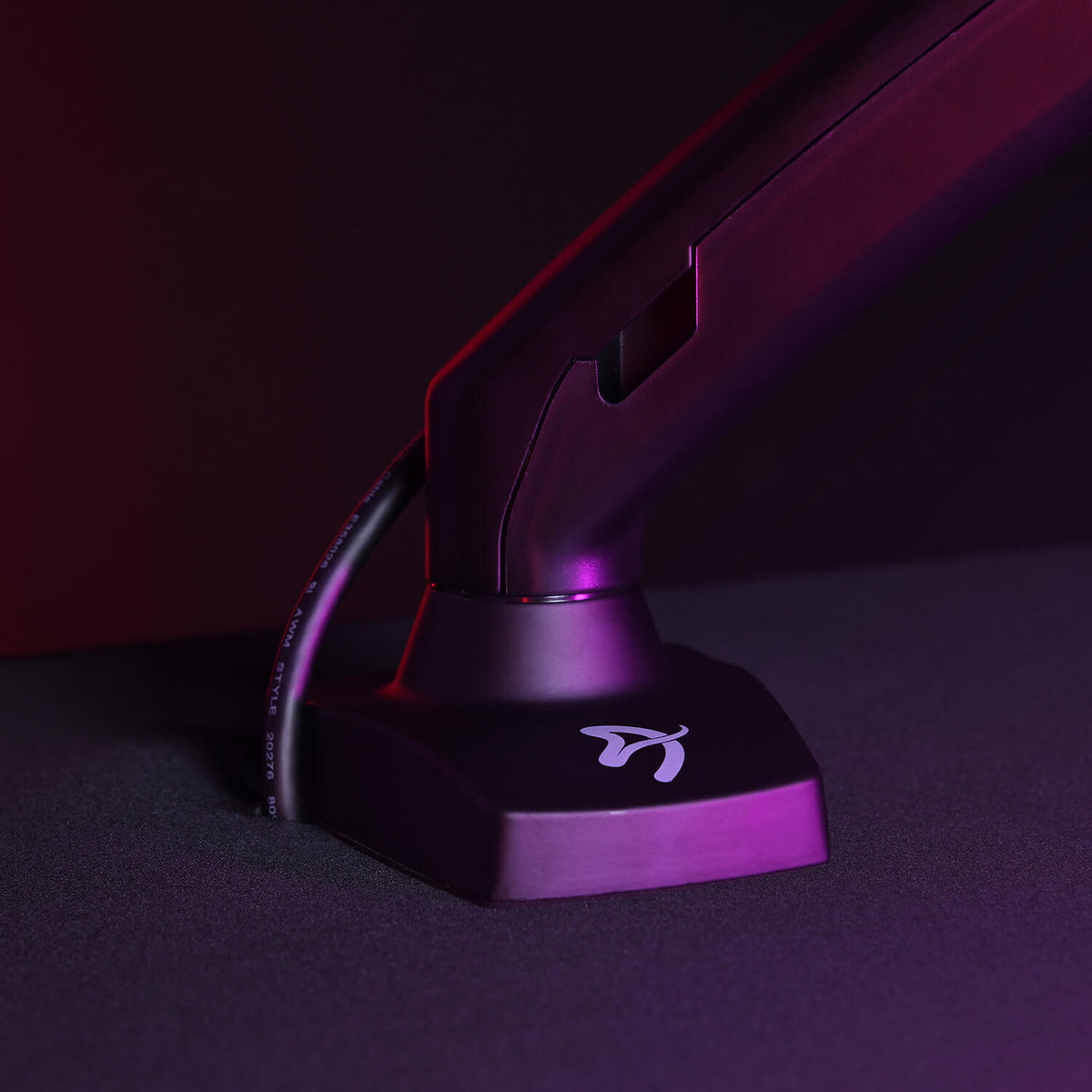 A purple monitor arm base with a logo, lit by pink and purple lighting.