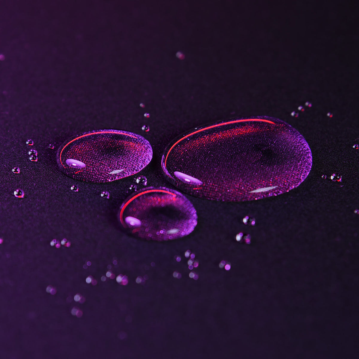 Purple water droplets on a dark surface with a soft, glowing light effect.