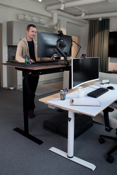Man working at a standing desk with dual monitors and office supplies visible.