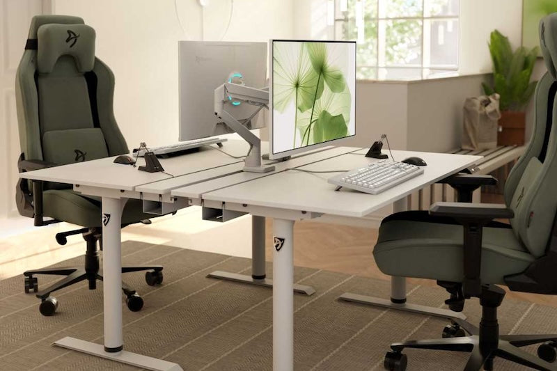 Modern office with two desks, computers, and green chairs on wheels, in a bright room.