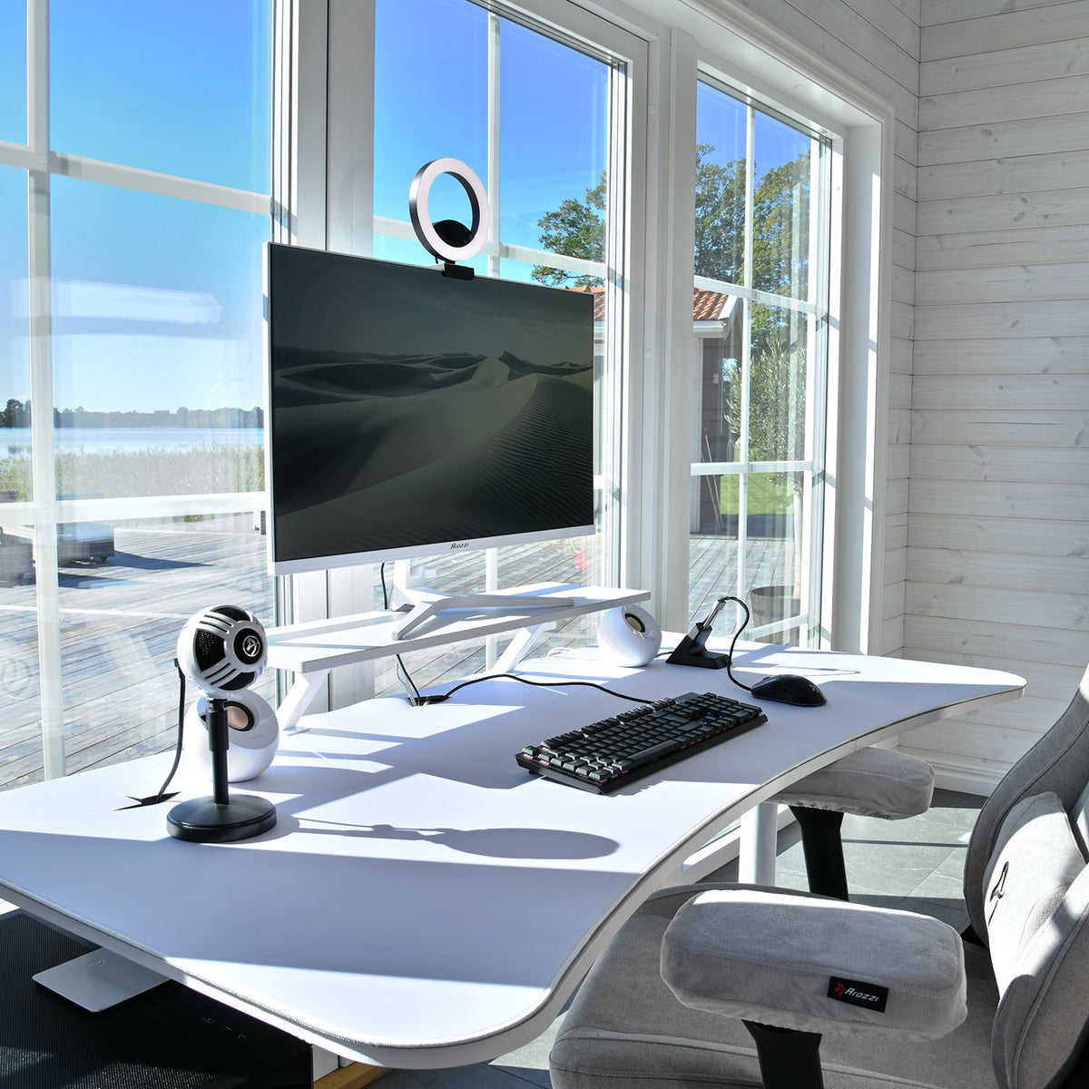 Modern desk setup with Arozzi Arena Mousepad, monitor, keyboard, mic by large sunny windows.