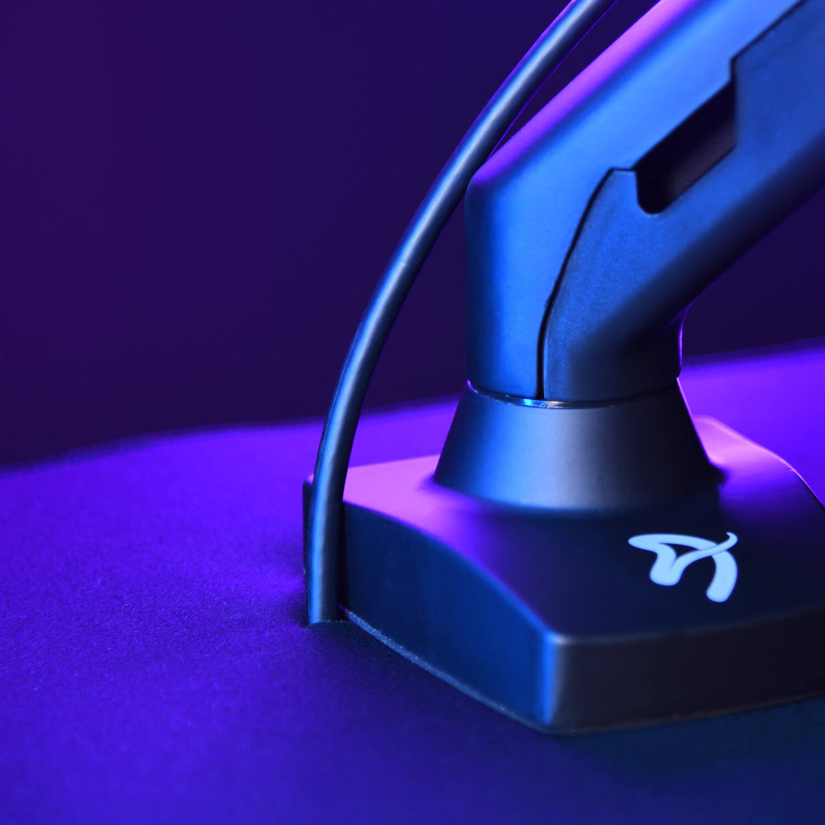 Close-up of a monitor stand base with a cable, illuminated by blue and purple light.