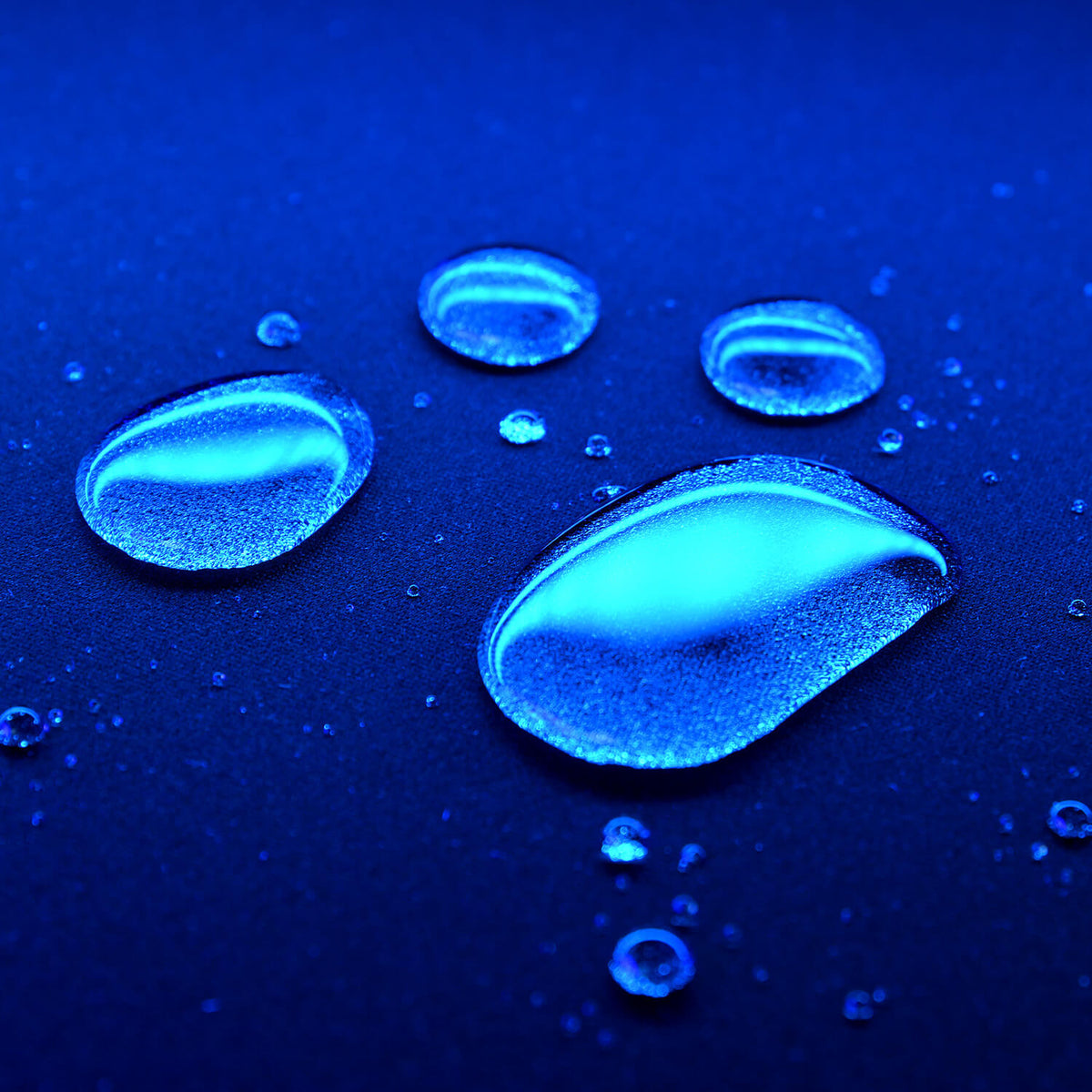 Blue water droplets on a dark surface, illuminated with reflective blue light.