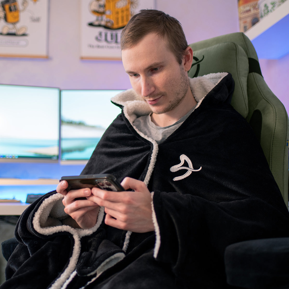 Man wears Arozzi Europe Chair Blanket hoodie, sitting in a chair and looking at his phone.