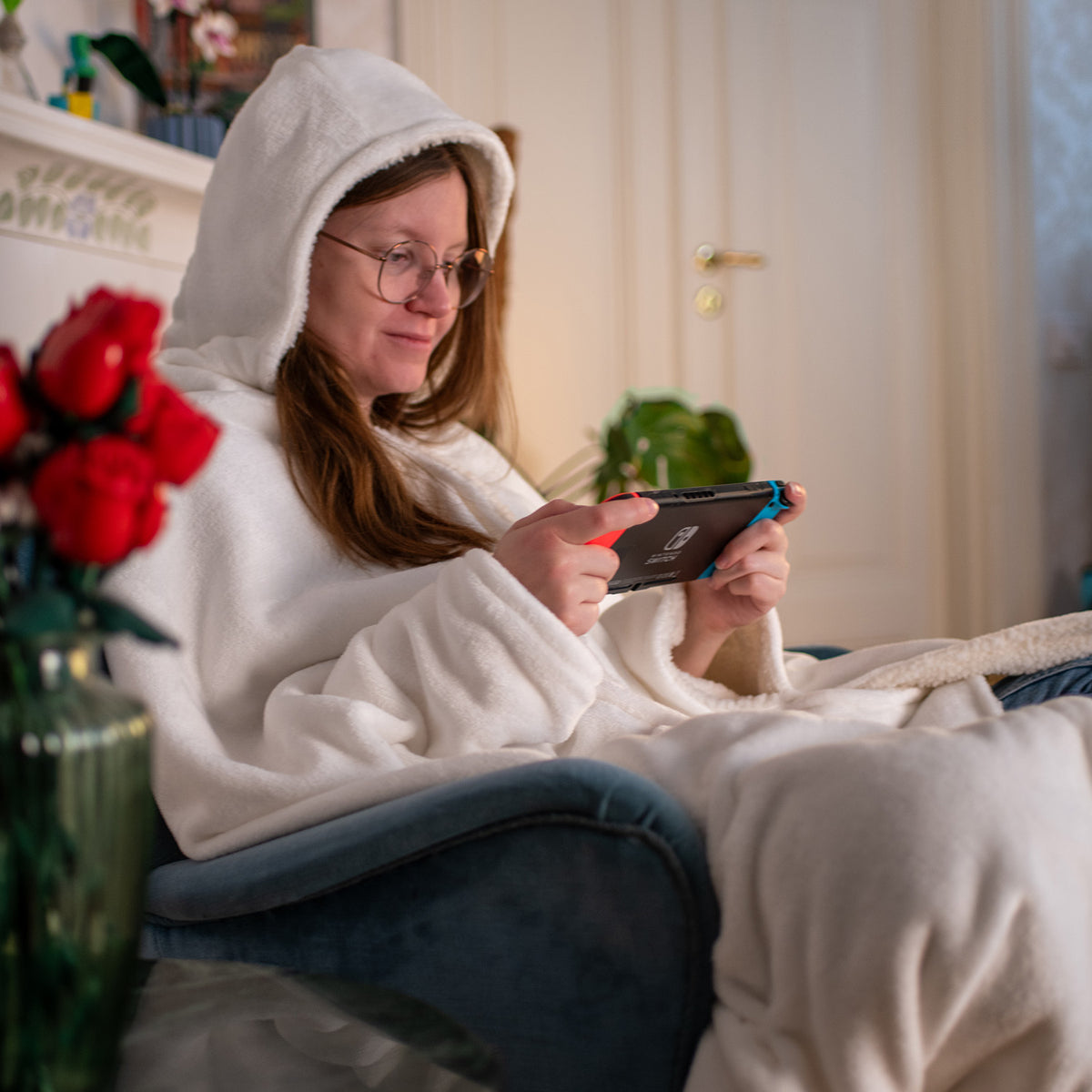 Woman in a white robe plays handheld games indoors, wrapped in an Arozzi Europe Chair Blanket.