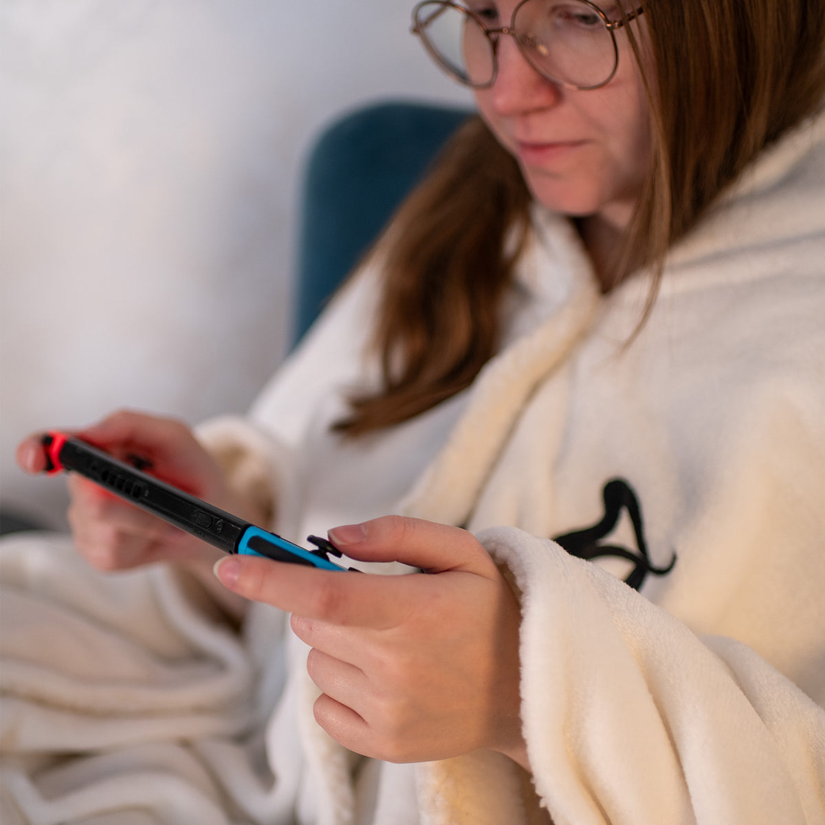 Gamer in glasses and robe enjoys Arozzi Europe Chair Blanket while playing on a handheld console.