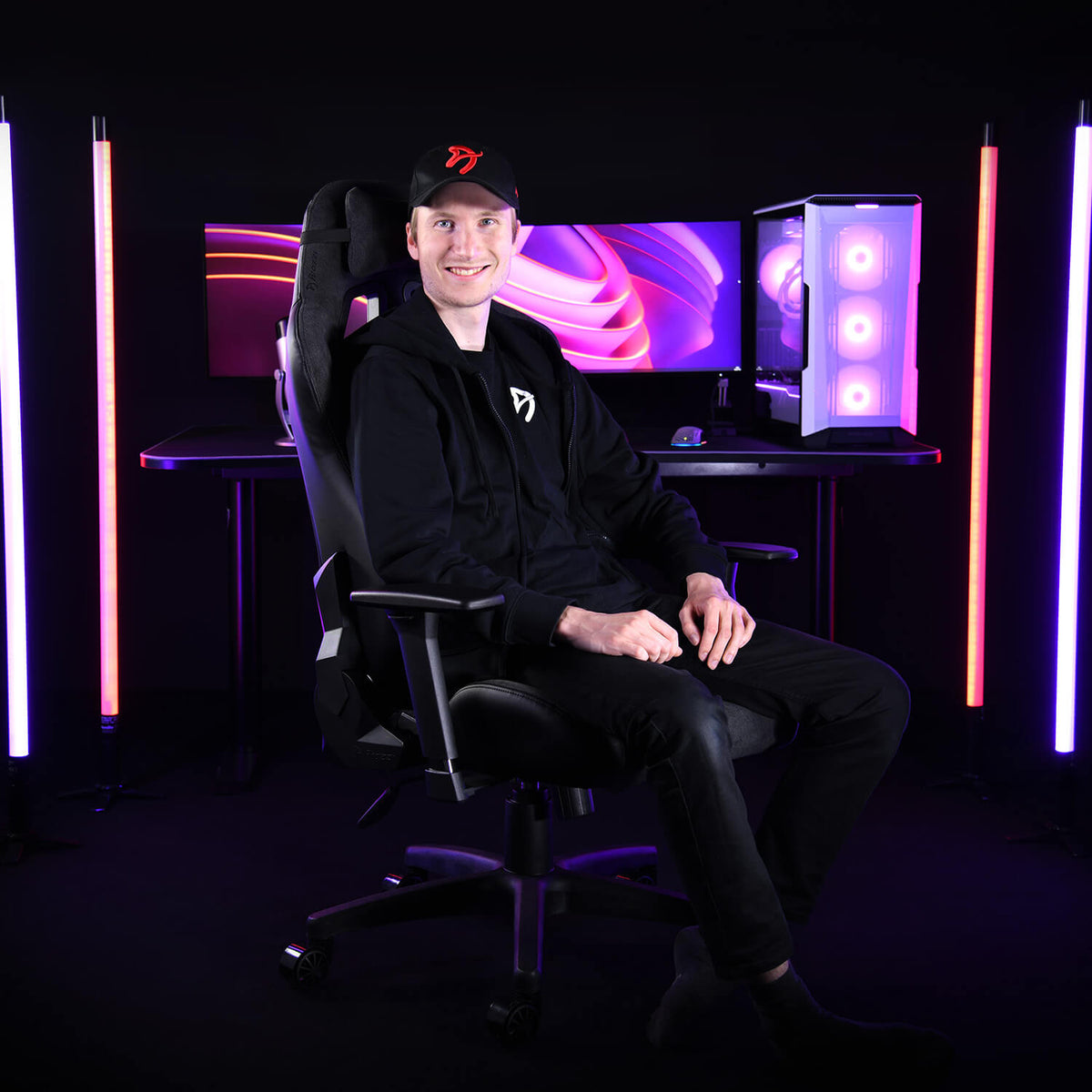 Smiling user in Arozzi Europe Avanti Soft Fabric chair, neon lights, PC setup, and monitors.