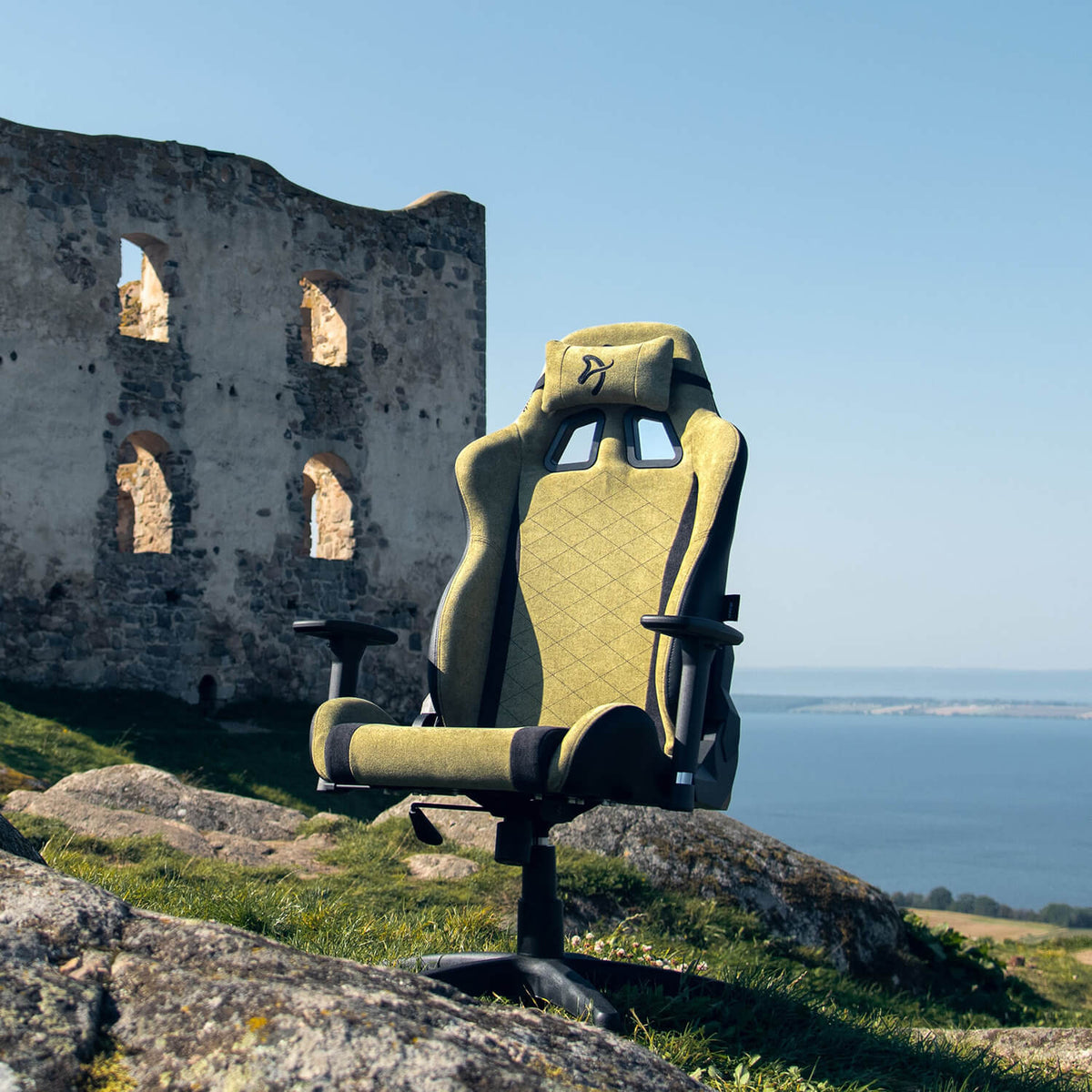 Arozzi Europe Avanti Soft Fabric chair with head pillow on rocky grass by ruins, sea and sky.