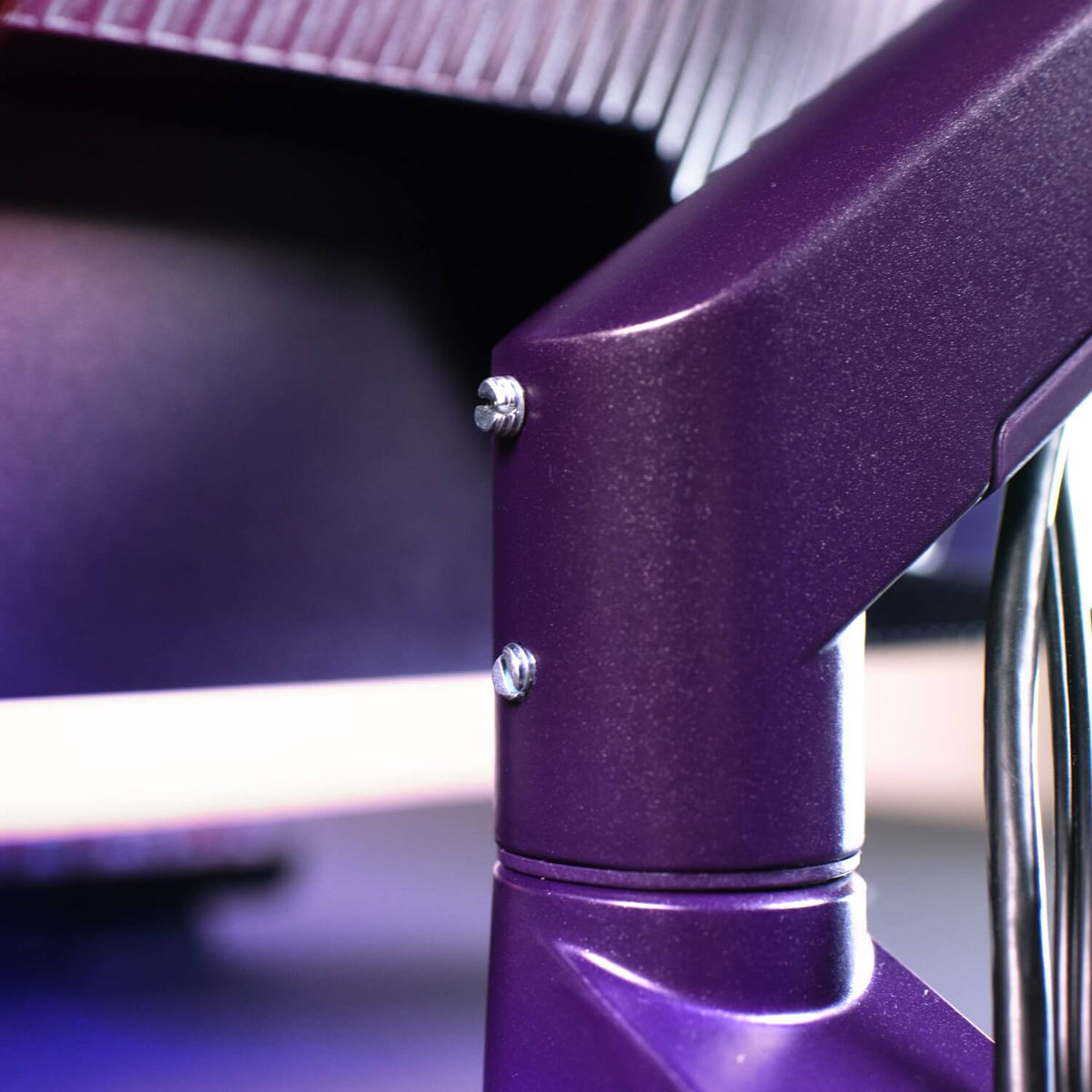Close-up of a purple metal monitor arm with visible screws and part of a screen in background.