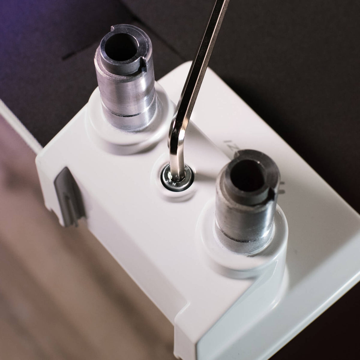 Allen wrench tightening a screw between two metal cylinders on a white plastic bracket.