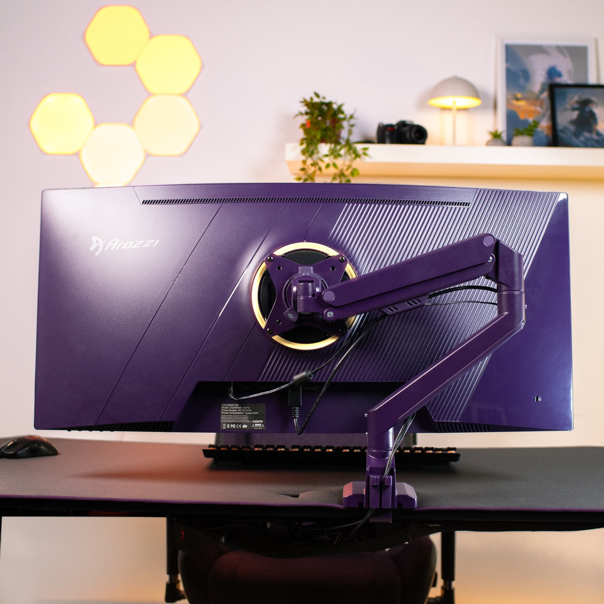 A purple Arozzi Europe Alzare Neo Single monitor arm sits on a desk with shelves and lights.