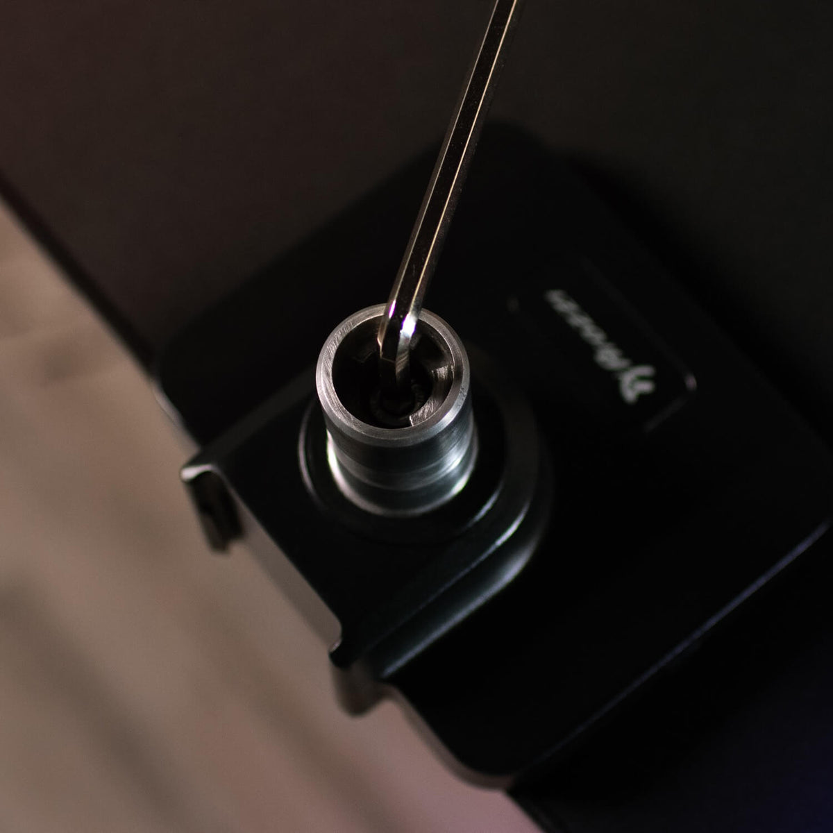 A hex key is inserted into a hex bolt on a black metal component.