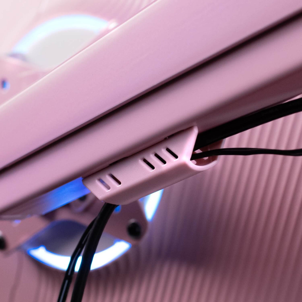 Close-up of pink cable clip holding wires on a light pink surface, with a glowing blue light.