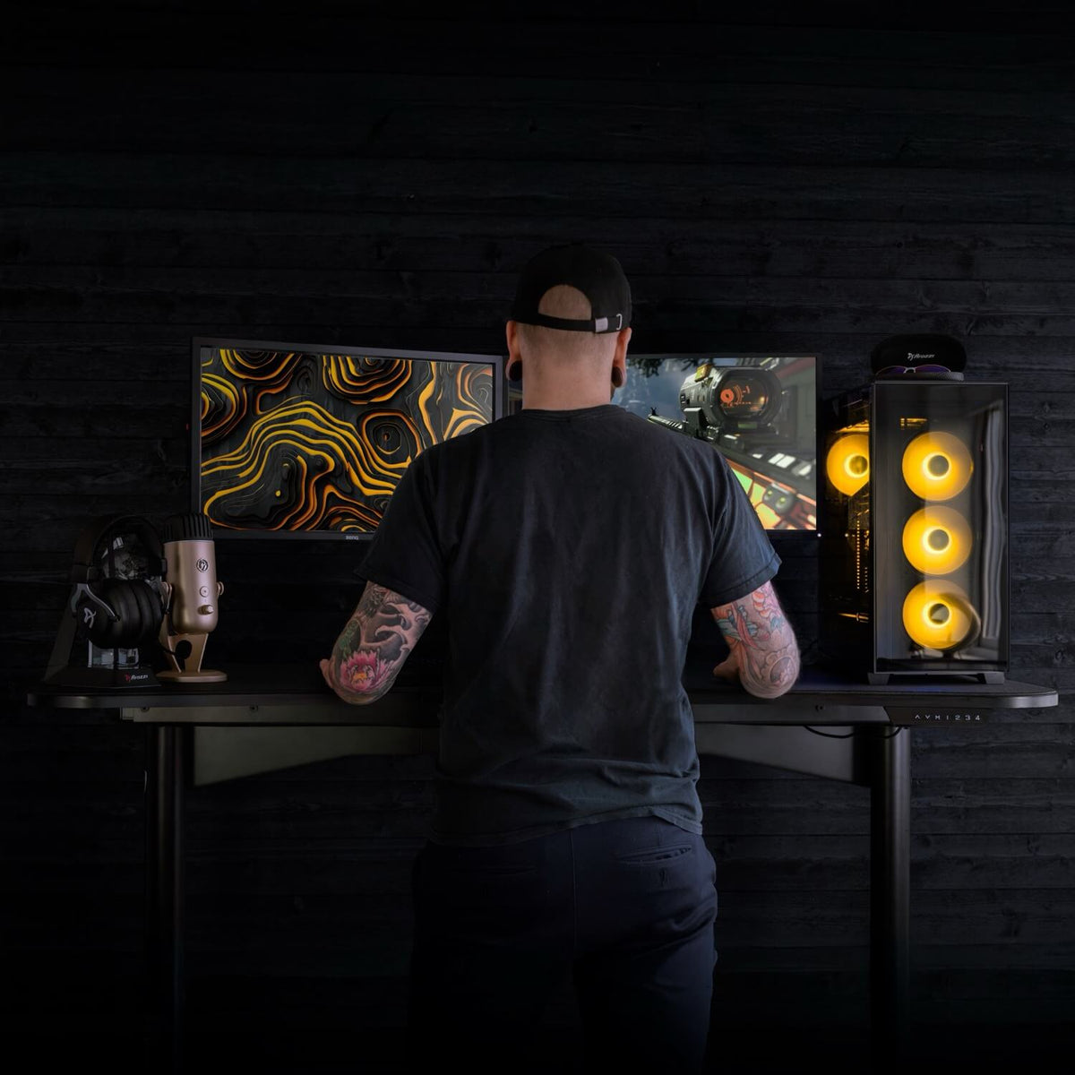 Tattooed gamer at Arozzi Arena Moto electric desk with yellow-lit PC in the setup.