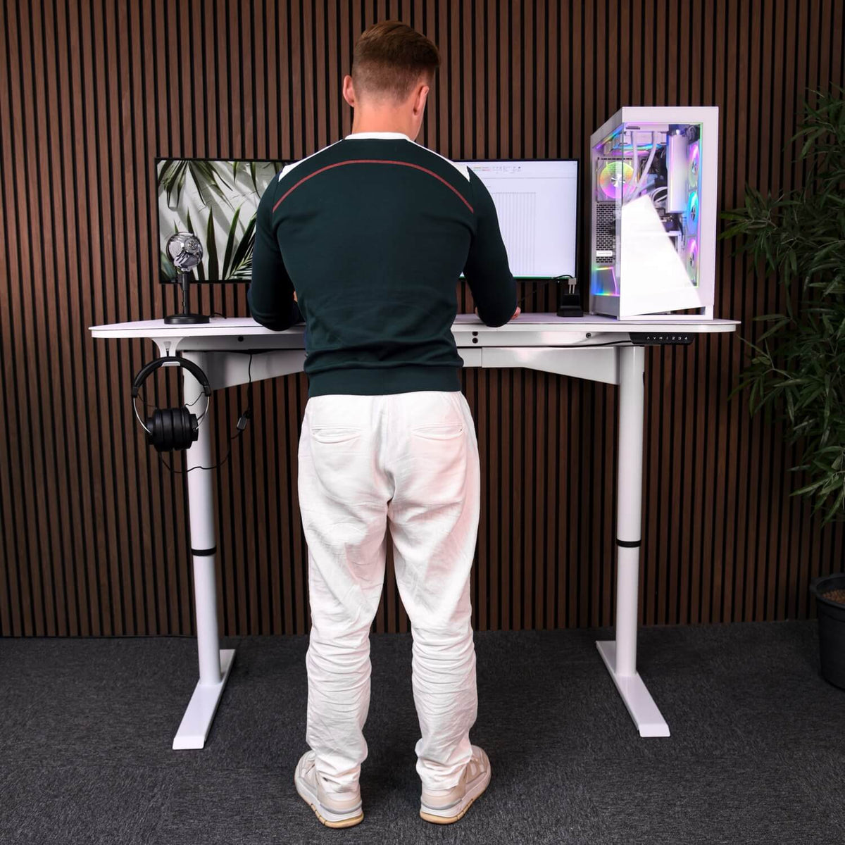 Person at an Arena Moto electric standing desk by Arozzi Europe with monitors in modern office.