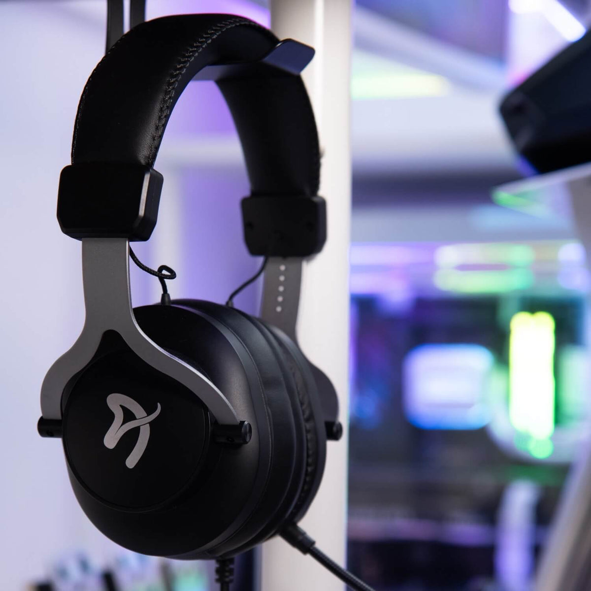 Aria Gaming Headset by Arozzi Europe, black over-ear with white logo, on stand, neon backdrop.