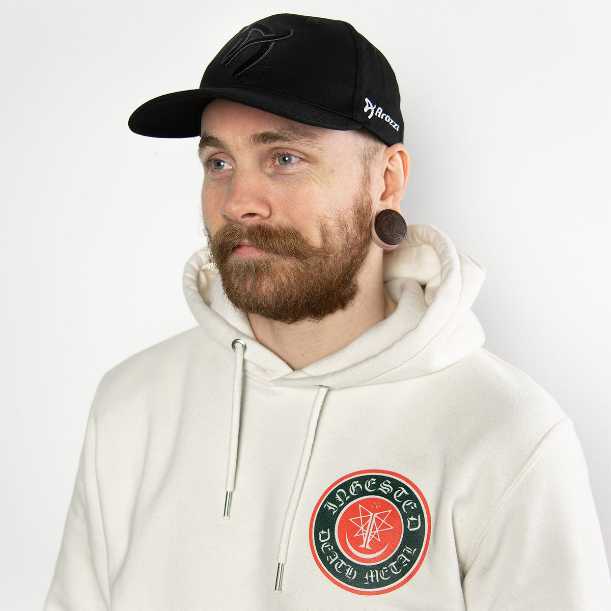 Man with beard in Arozzi Europe Sport Cap, white hoodie, plain white background.