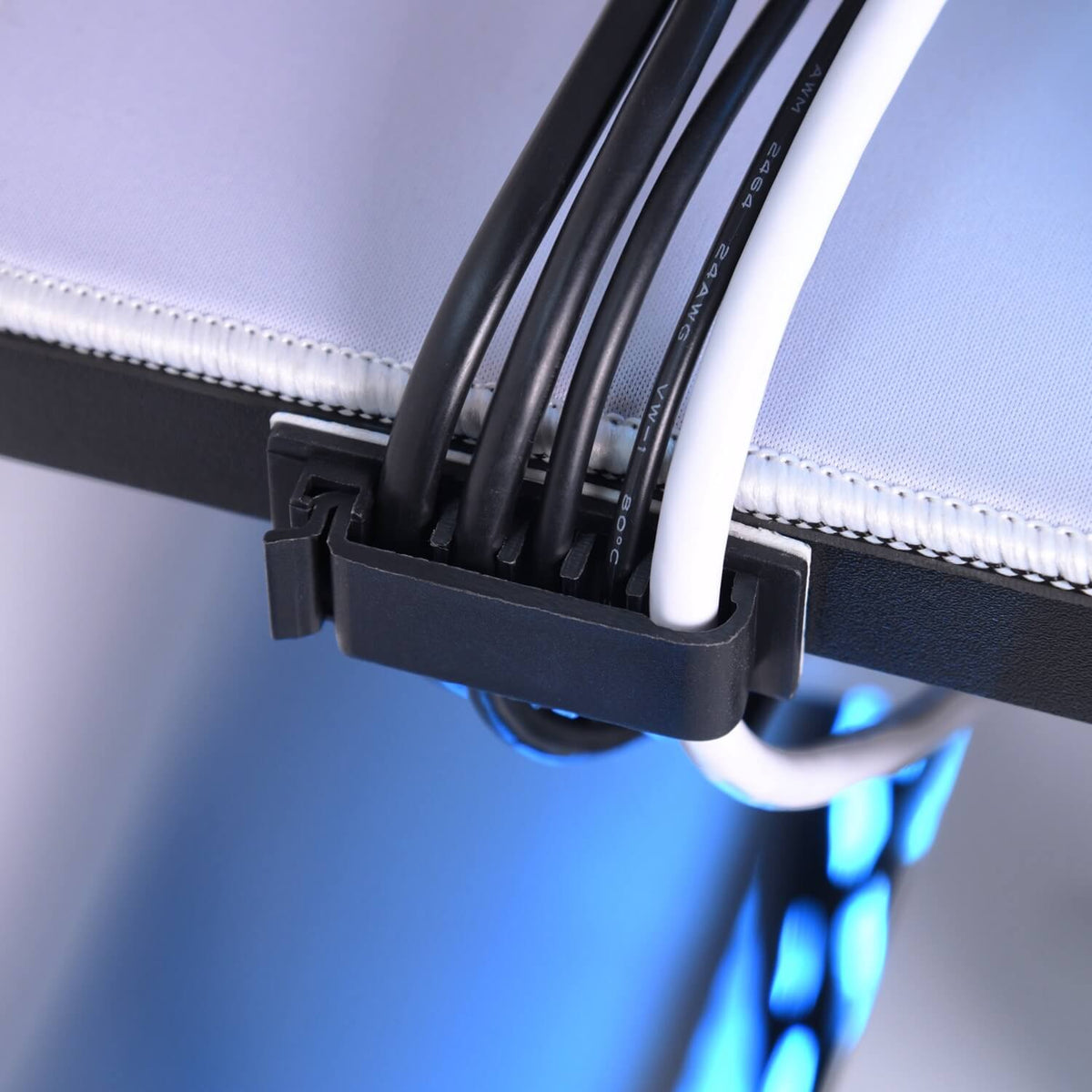 Black and white cables held by a clip attached to the edge of a desk, with blue lighting behind.