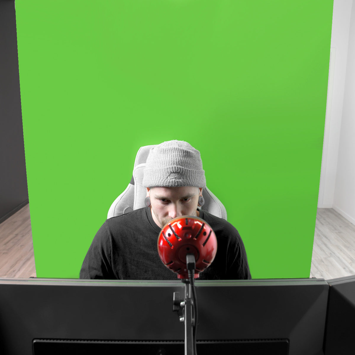 Person at desk with red mic, Arozzi Europe Green Screen behind them.
