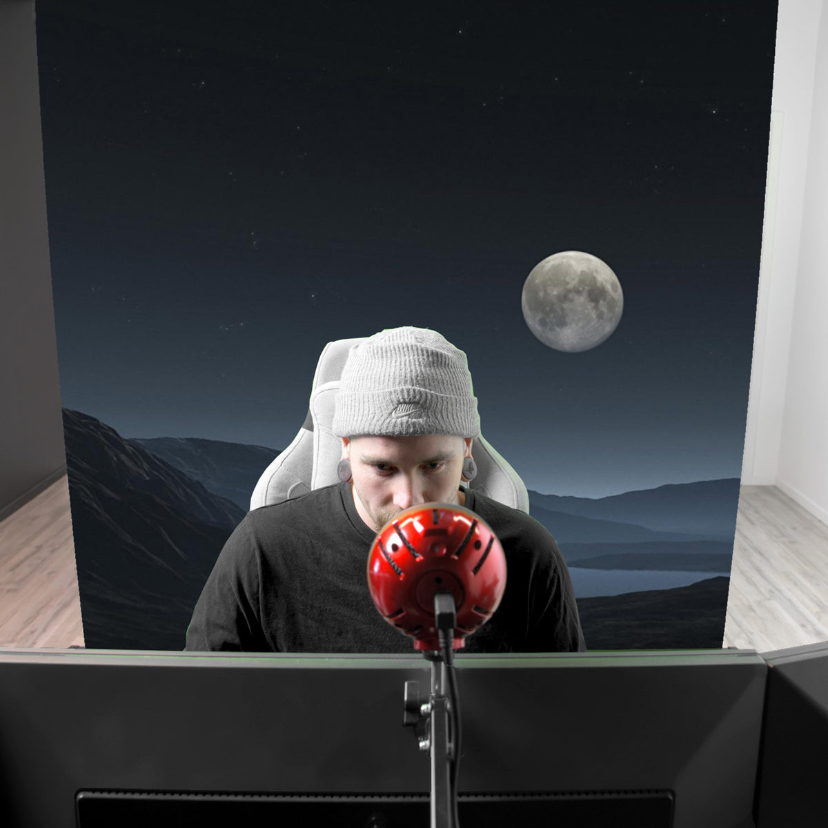 Man with gray beanie at desk, red mic, Arozzi Europe Green Screen shows moonlit night backdrop.