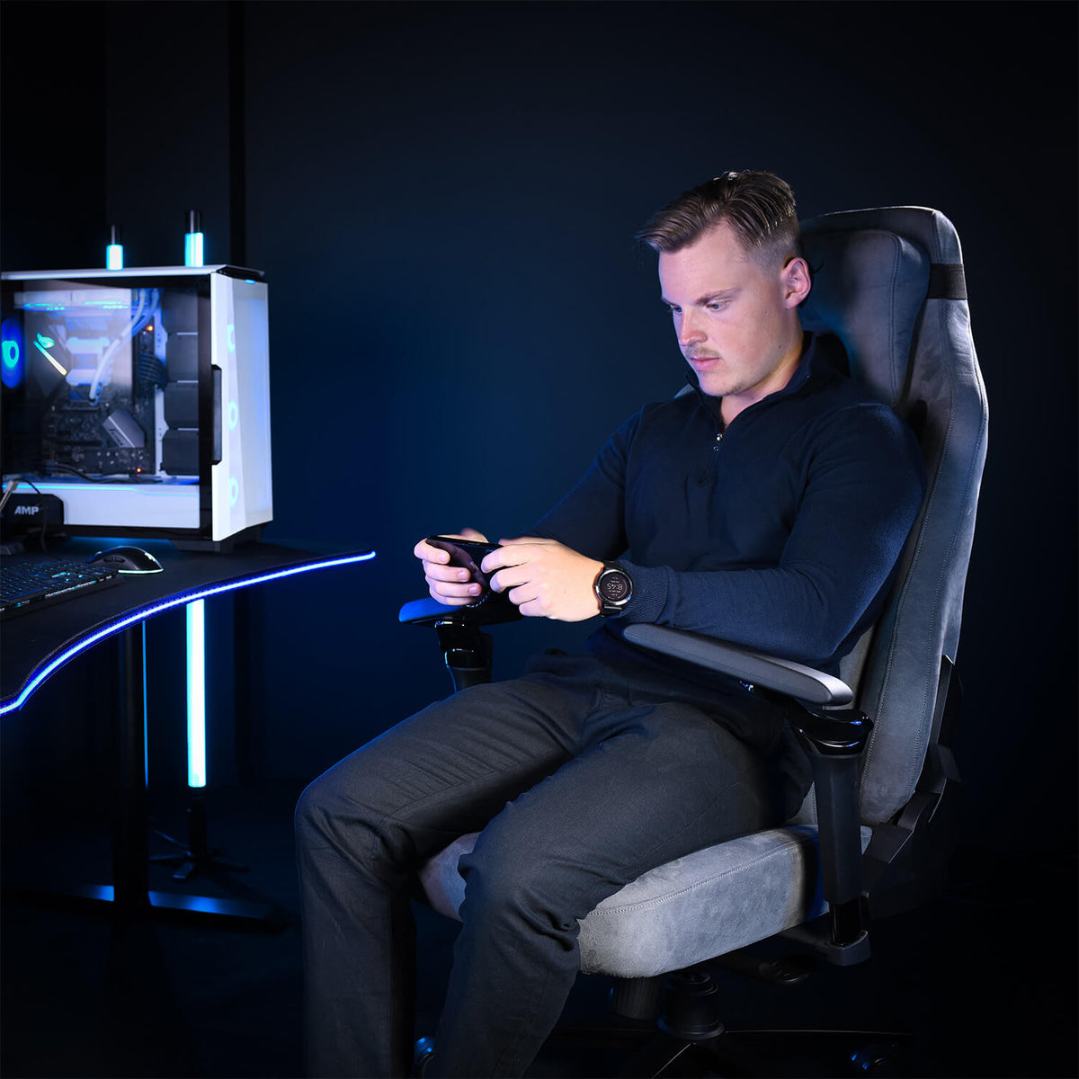 Man in black in Arozzi Europe chair with Infinity Armrests, on phone near blue-lit PC.
