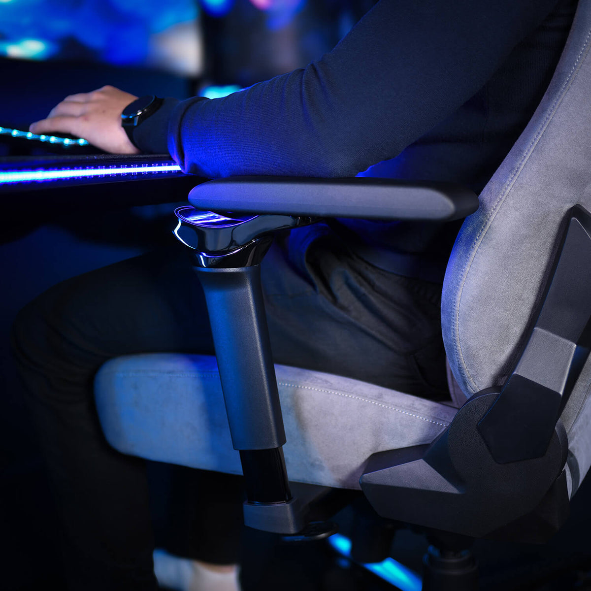 Person sits in a gray Arozzi Europe chair with Infinity Armrests, typing at a glowing desk.