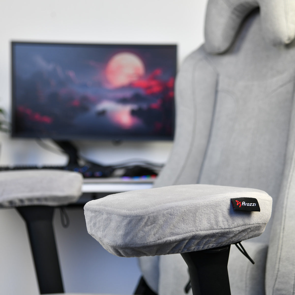 Gray gaming chair with Arozzi Europe Memory Foam Armrest Pads, blurred monitor in background.
