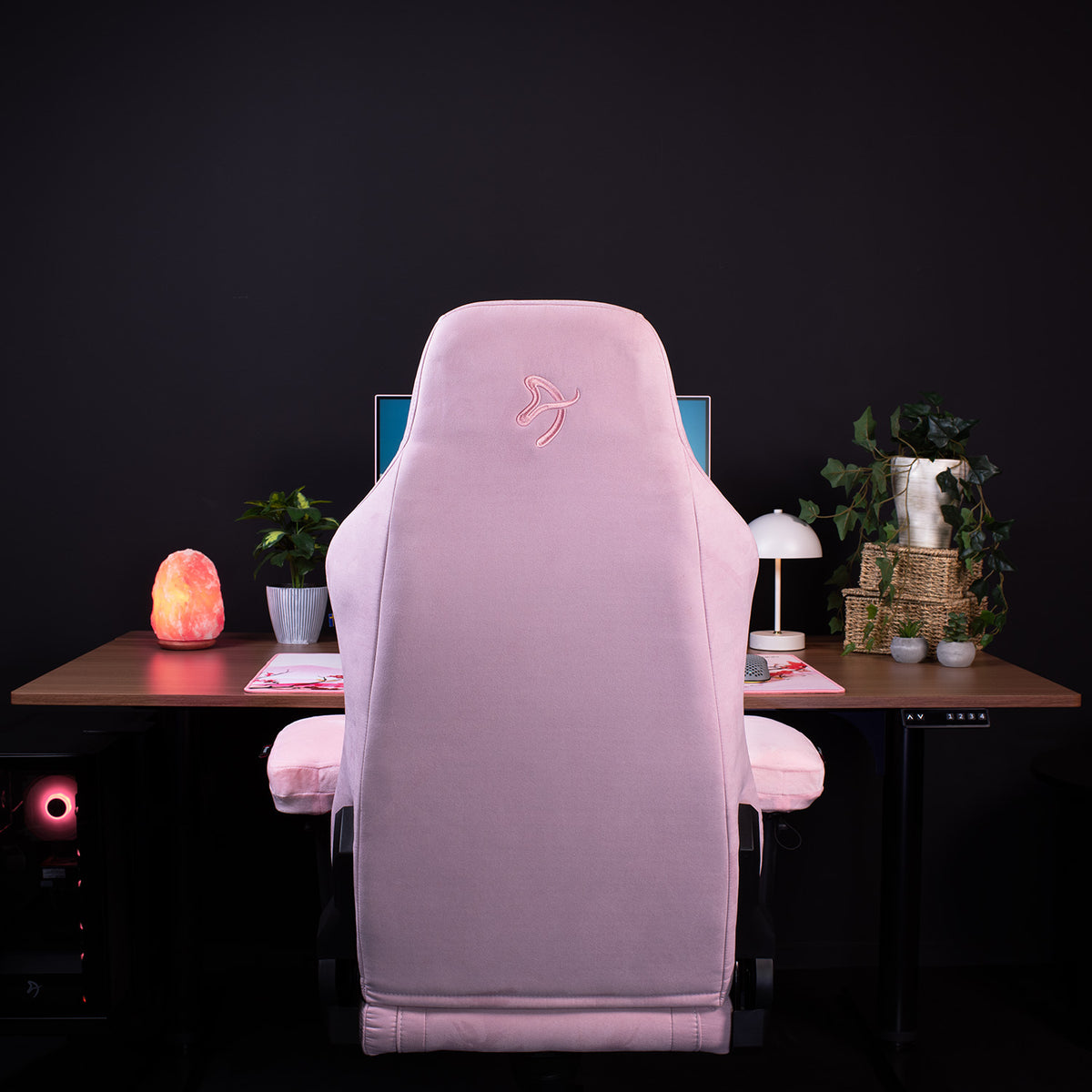 A pink gaming chair with Arozzi Europe’s Memory Foam Armrest Pads sits by a desk with plants.
