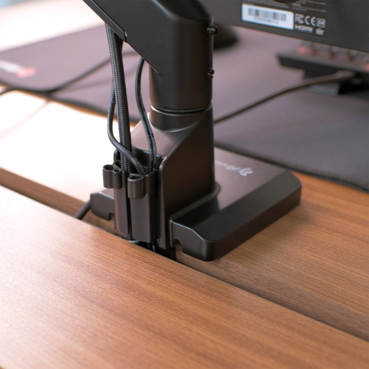 Black monitor arm mounted on a wooden desk, with cables neatly organized behind it.