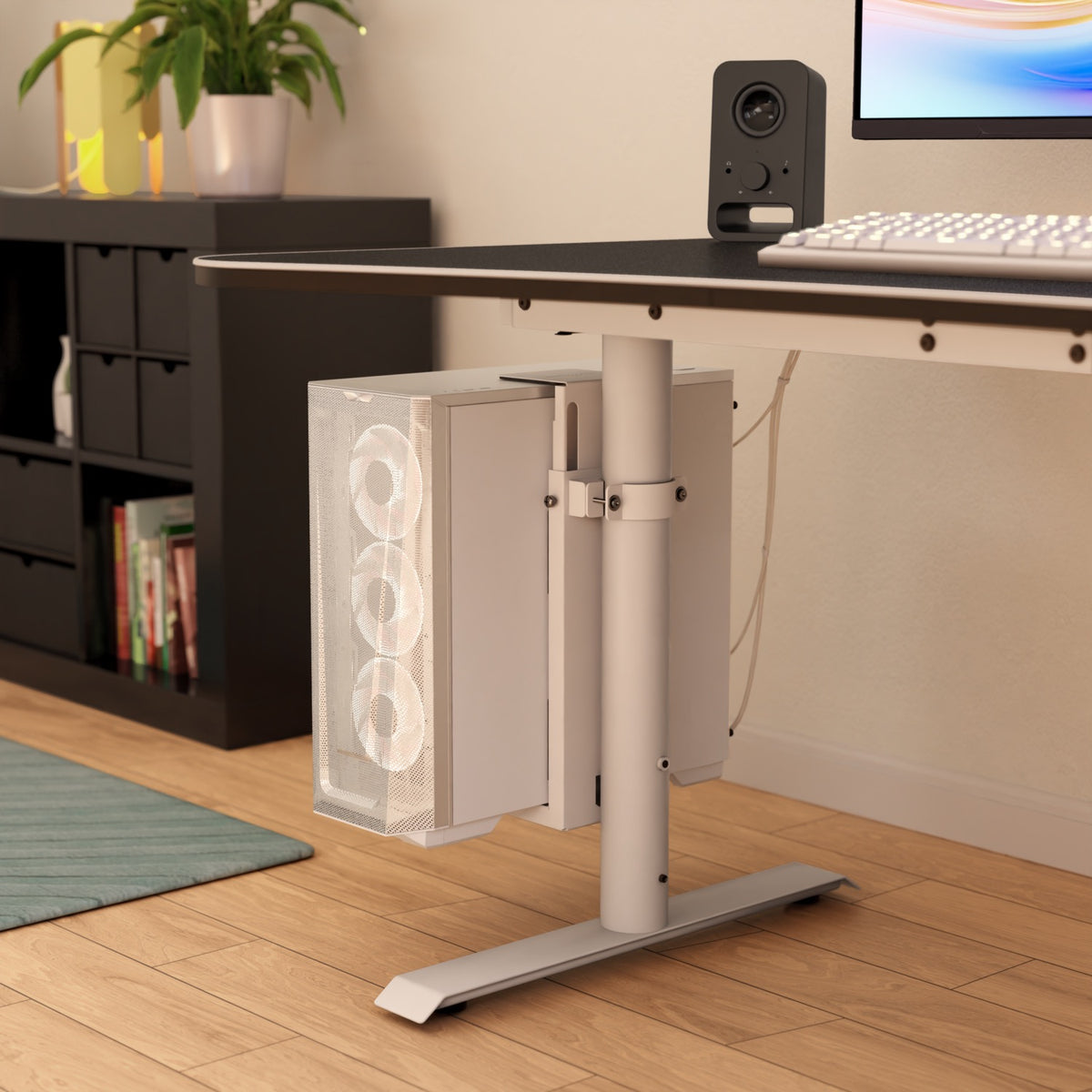 A white PC case in an Arozzi Europe Arena PC Mount sits under a desk by a speaker and monitor.