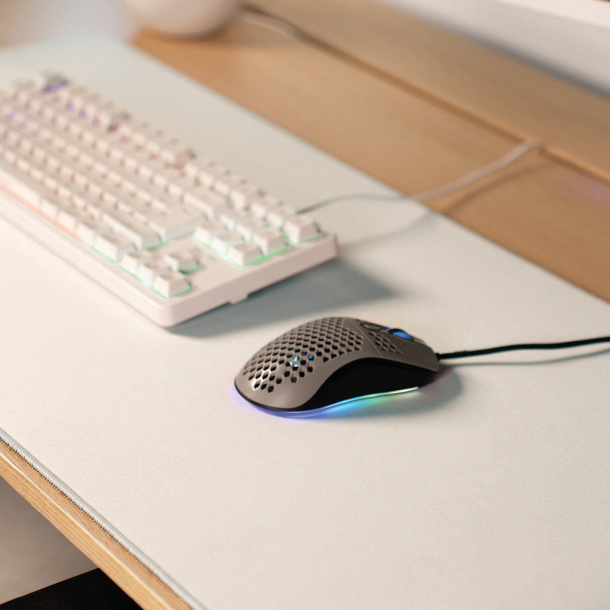 A white keyboard, wired RGB mouse, and Arozzi Zona Mousepad on a light-colored desk.