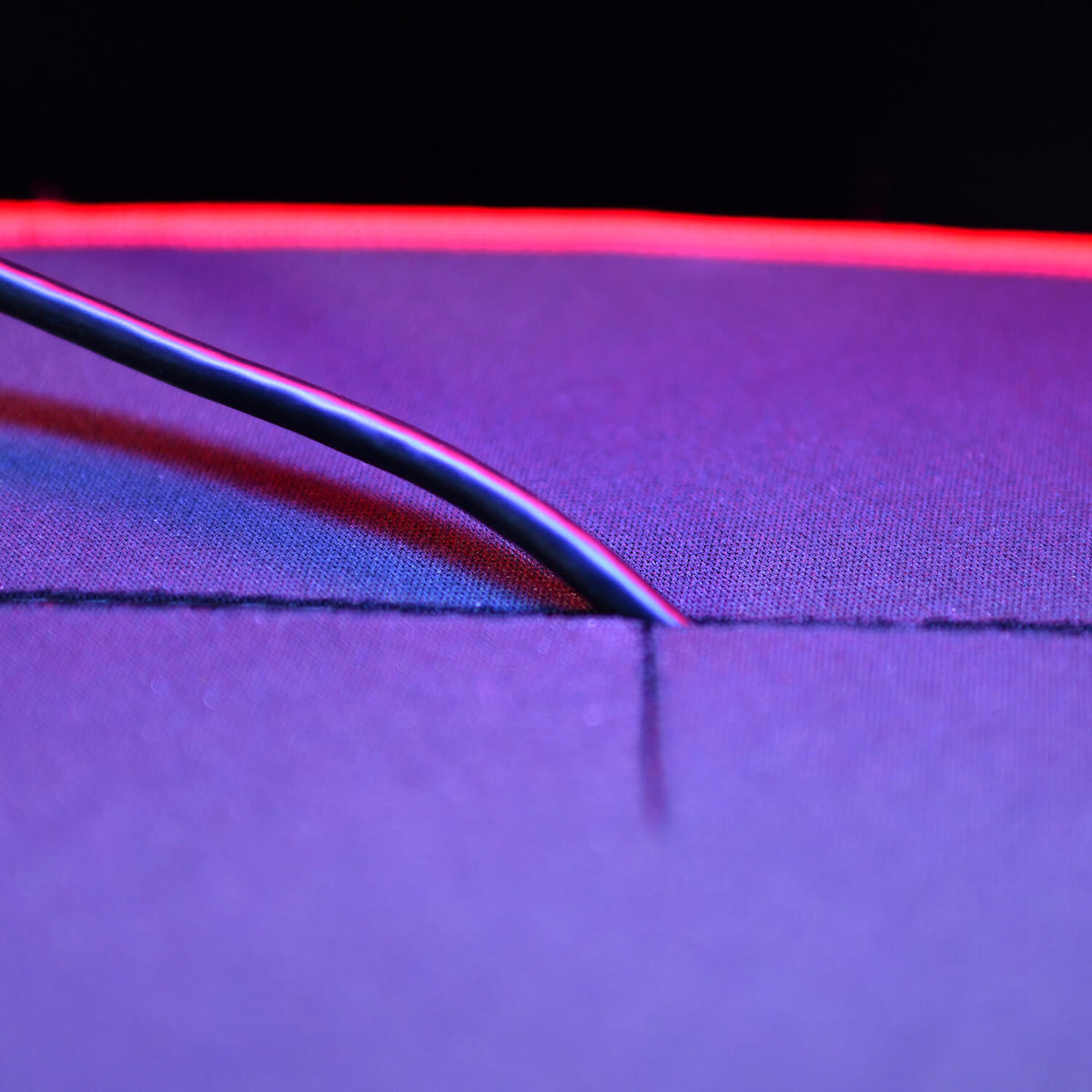 A black cable on a purple surface with a red light in the background.