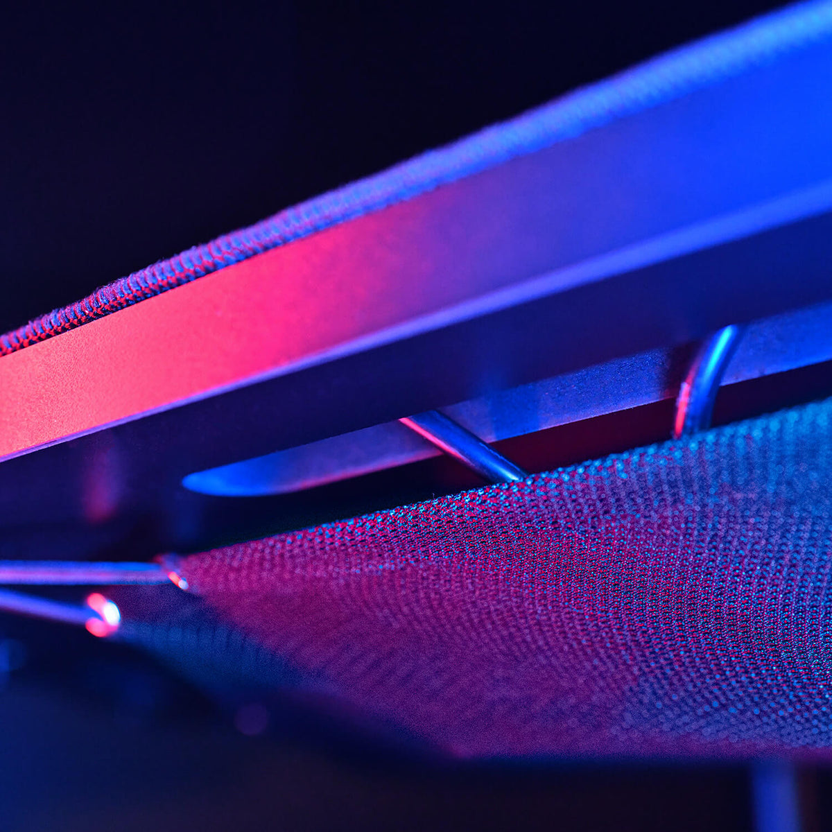 Close-up of a textured object lit with blue and pink lighting, featuring metal supports.