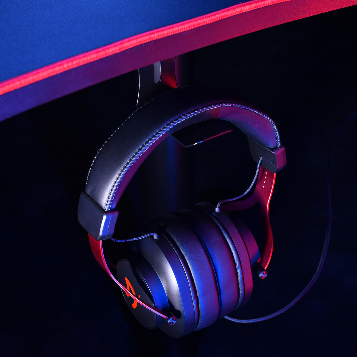 Black headphones hanging under a desk with a red edge, illuminated by neon lighting.