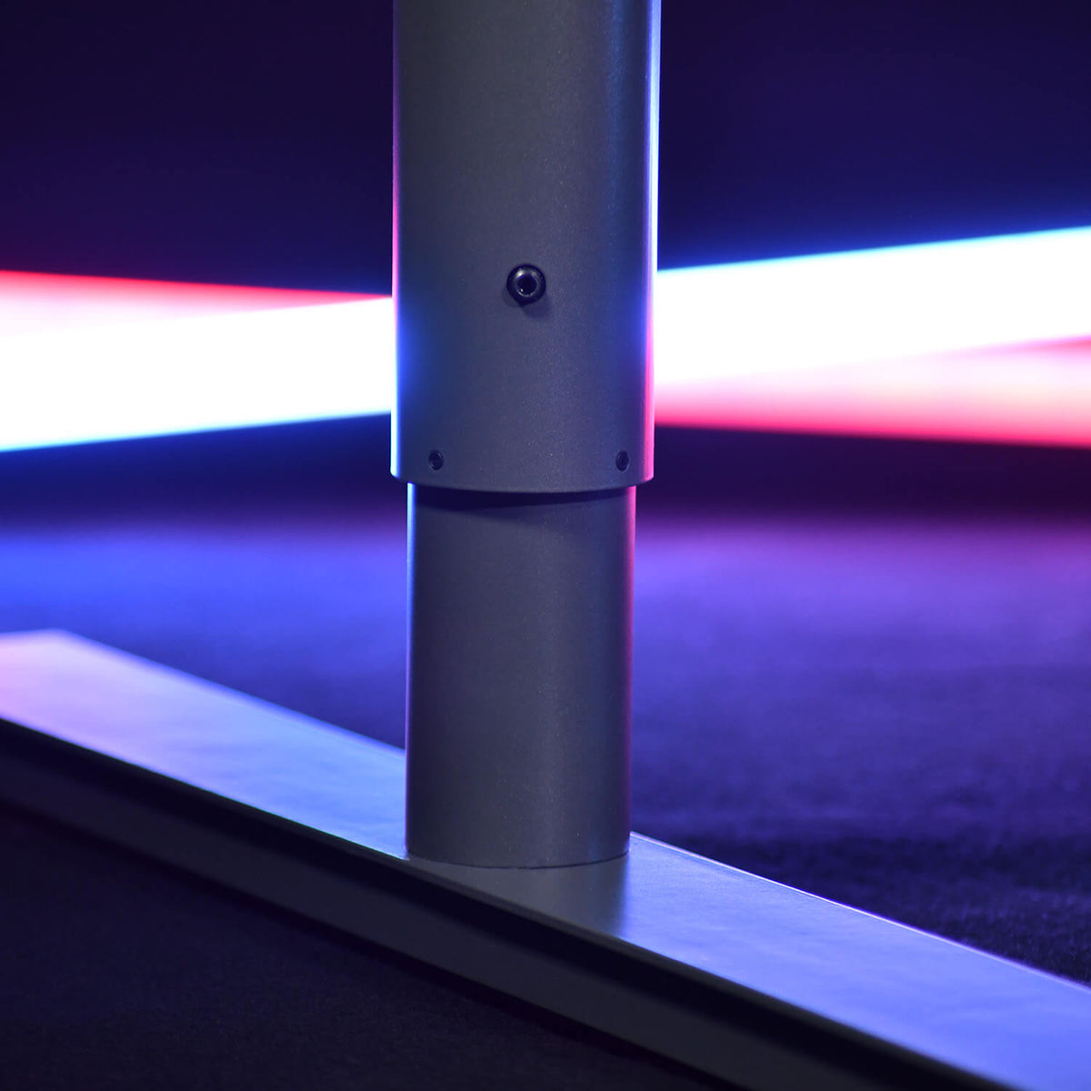 Close-up of a metal pole base with blurred red and blue lights in the background.